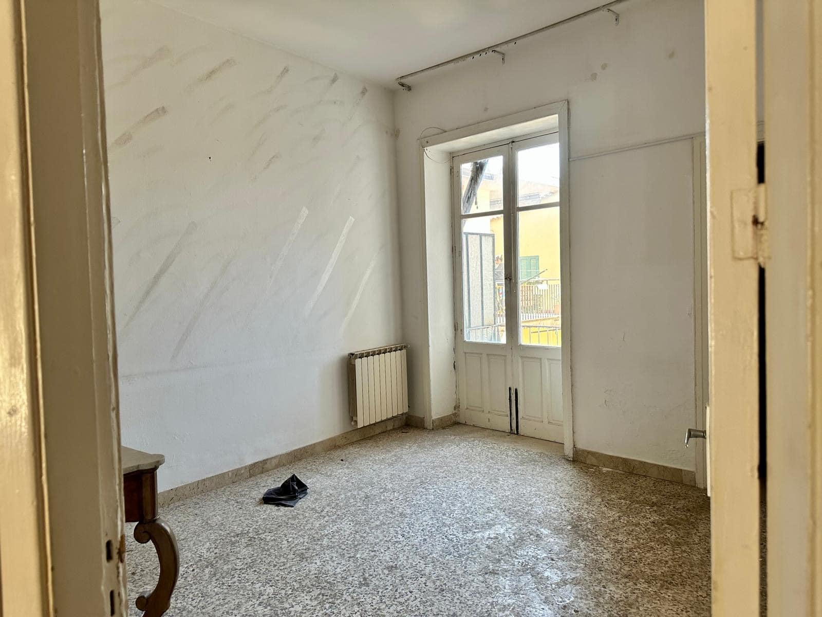 Affaccio su una stanza vuota in fase di ristrutturazione con pareti bianche, parquet e grande finestra che permette l'ingresso di molta luce naturale, ideale per una futura abitazione.