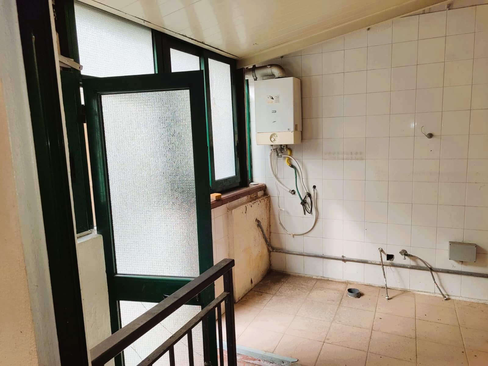 Balcone in fase di ristrutturazione con impianto di acqua e riscaldamento, pavimentazione in piastrelle e finestra con vetri opachi per privacy e luce naturale, ideale per interventi di ristrutturazione casa.