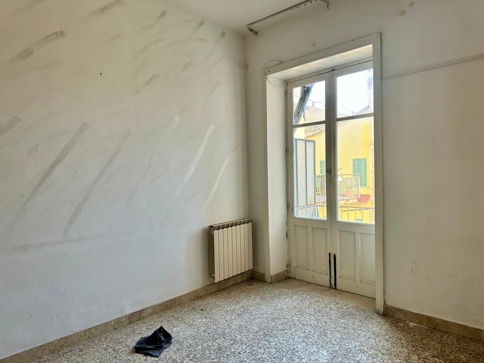 Finestra grande in un appartamento vuoto con pareti bianche, pavimento in marmo colorato e radiatore visibile, luce naturale che entra dall'esterno, ambiente da ristrutturare, immobile da ristrutturare, soluzione abitativa a Roma, NextCasa.