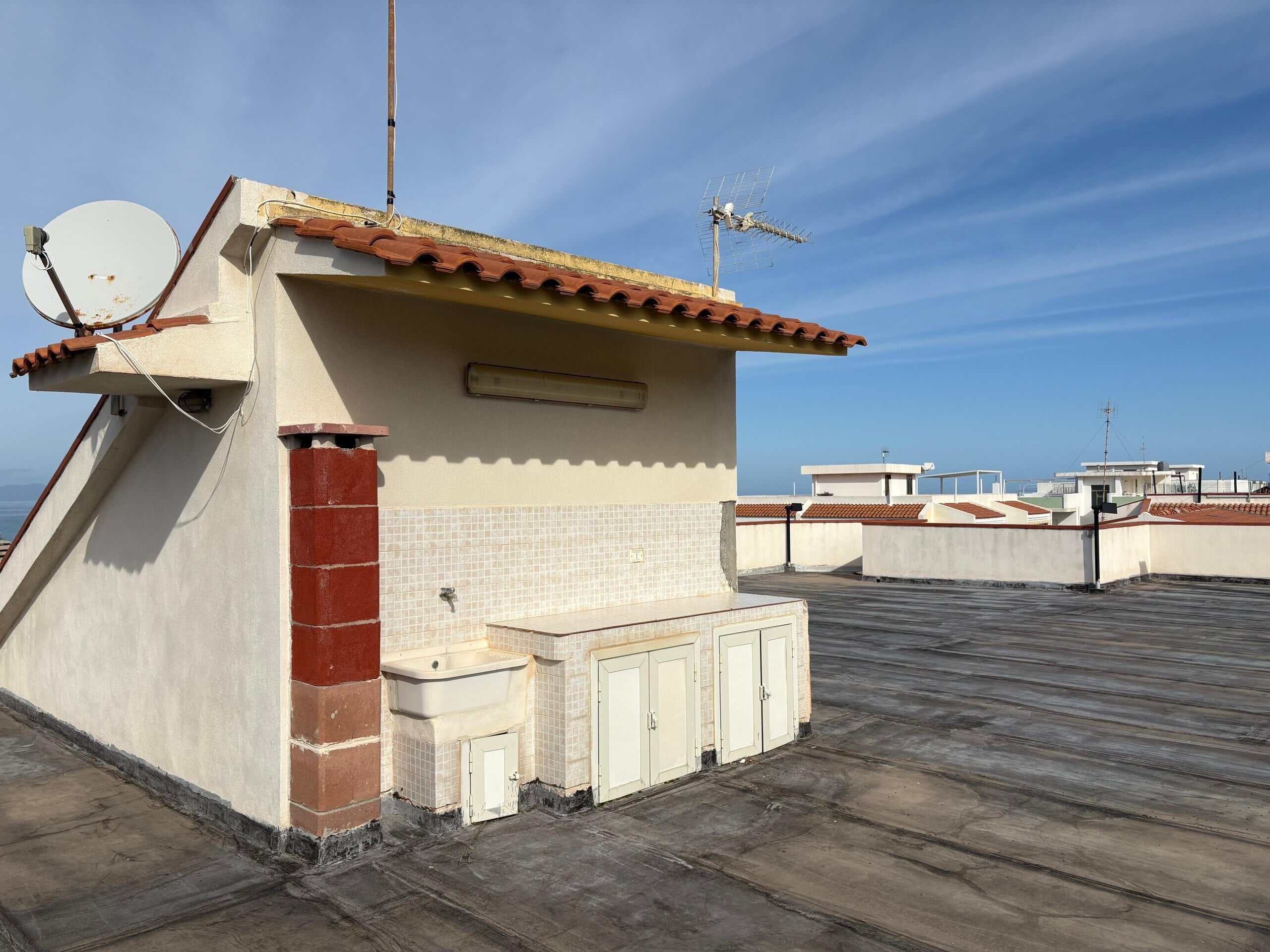 Ampio terrazzo su casa con vista sul cielo, coperto da uno strato di tegole rosse e attrezzato con antenna satellitare, lavabo e moduli di stoccaggio. Ideale per rilassarsi e godersi il panorama.