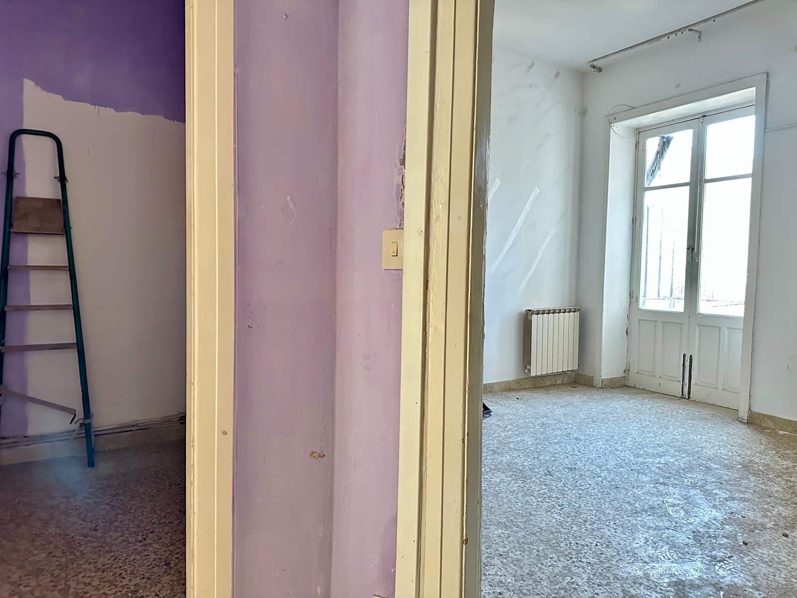 Locale da ristrutturare con pareti bianche e lilla, grande finestra che permette l'ingresso di molta luce naturale, riscaldamento a radiatori, pavimento in gres porcellanato, possibilità di personalizzazione.