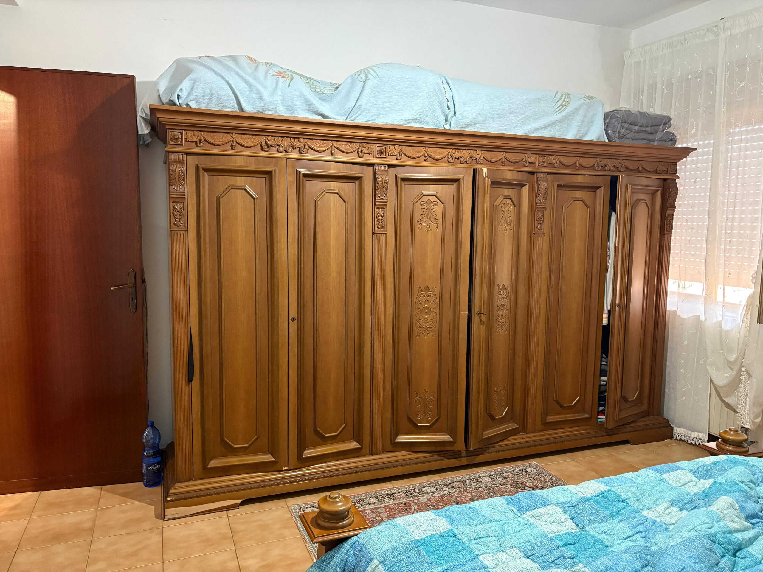 Armadio in legno massello antico con dettagli artigianali e vano sopra il letto, in stile classico e rustico, ideale per arredare camere da letto eleganti e tradizionali.