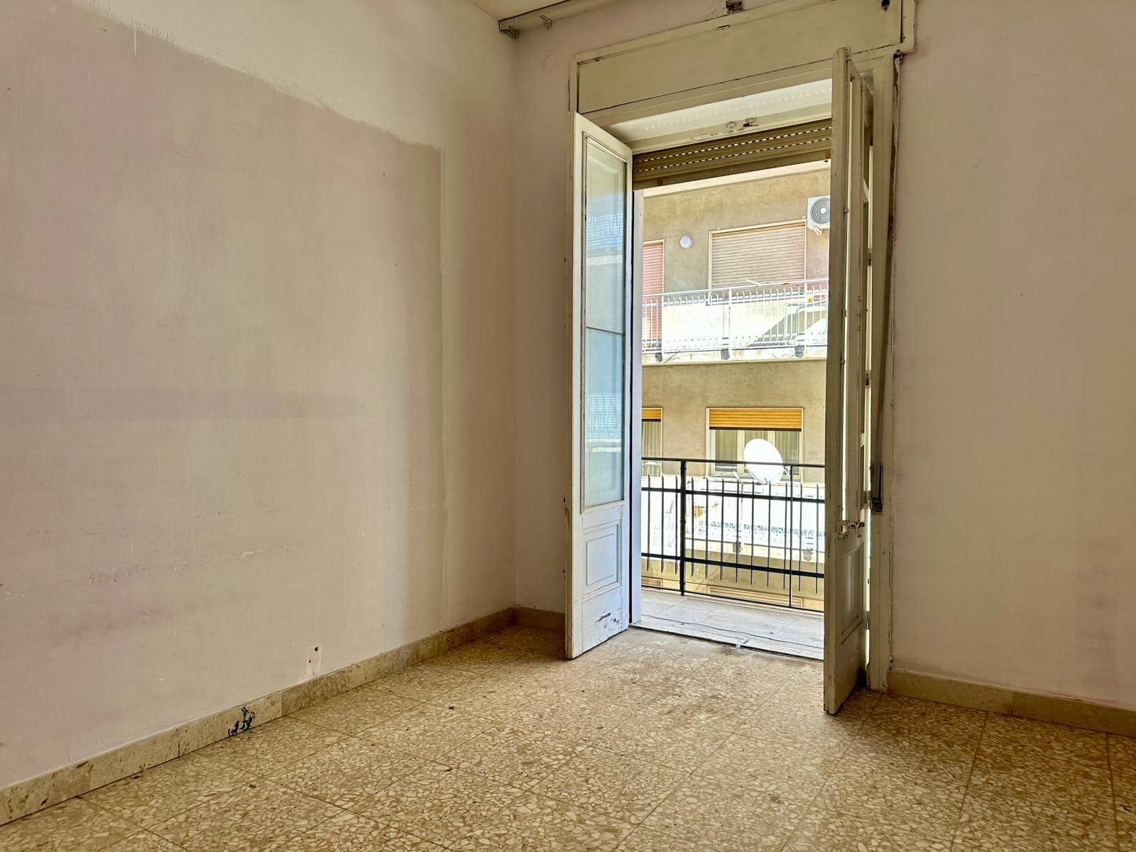 Finestra con balcone in appartamento in affitto, vista esterna su edificio e strada, interni vuoti con pareti bianche e pavimento in marmo beige.