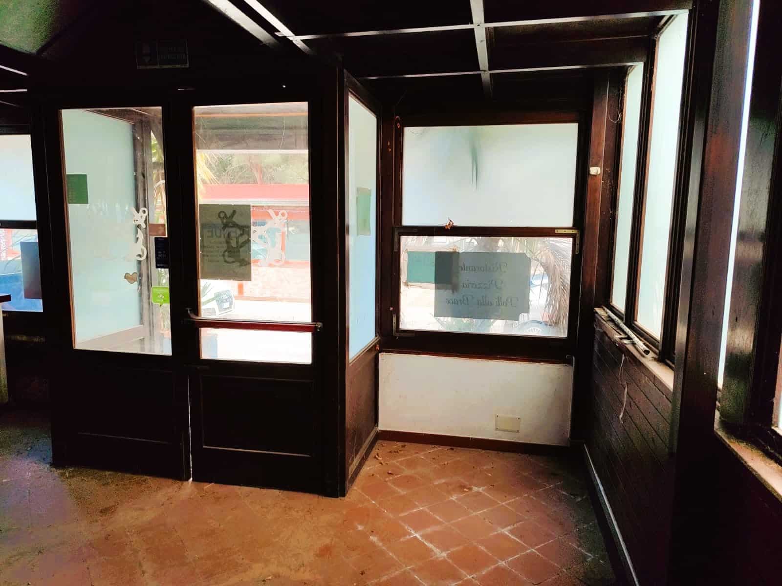 Finestra e porta in legno con vetri trasparenti, ambiente interno con pavimentazione in piastrelle, finestra con etichette promozionali e decorazioni, illuminazione naturale, ideale per investimento immobiliare.