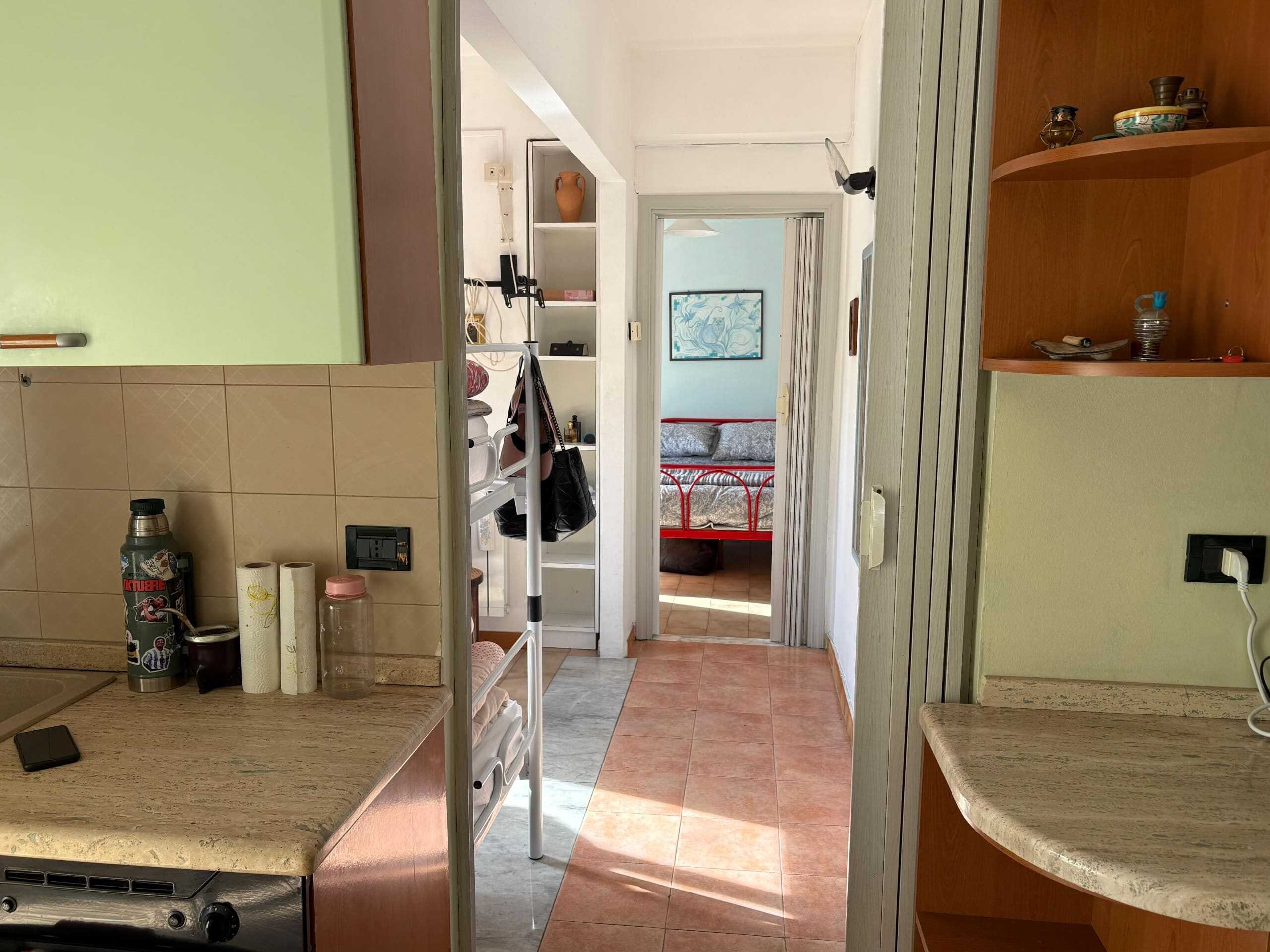 Immagine di un interno di appartamento con cucina e zona notte, vista dalla cucina verso il soggiorno, con dettagli di arredamento e oggetti domestici.