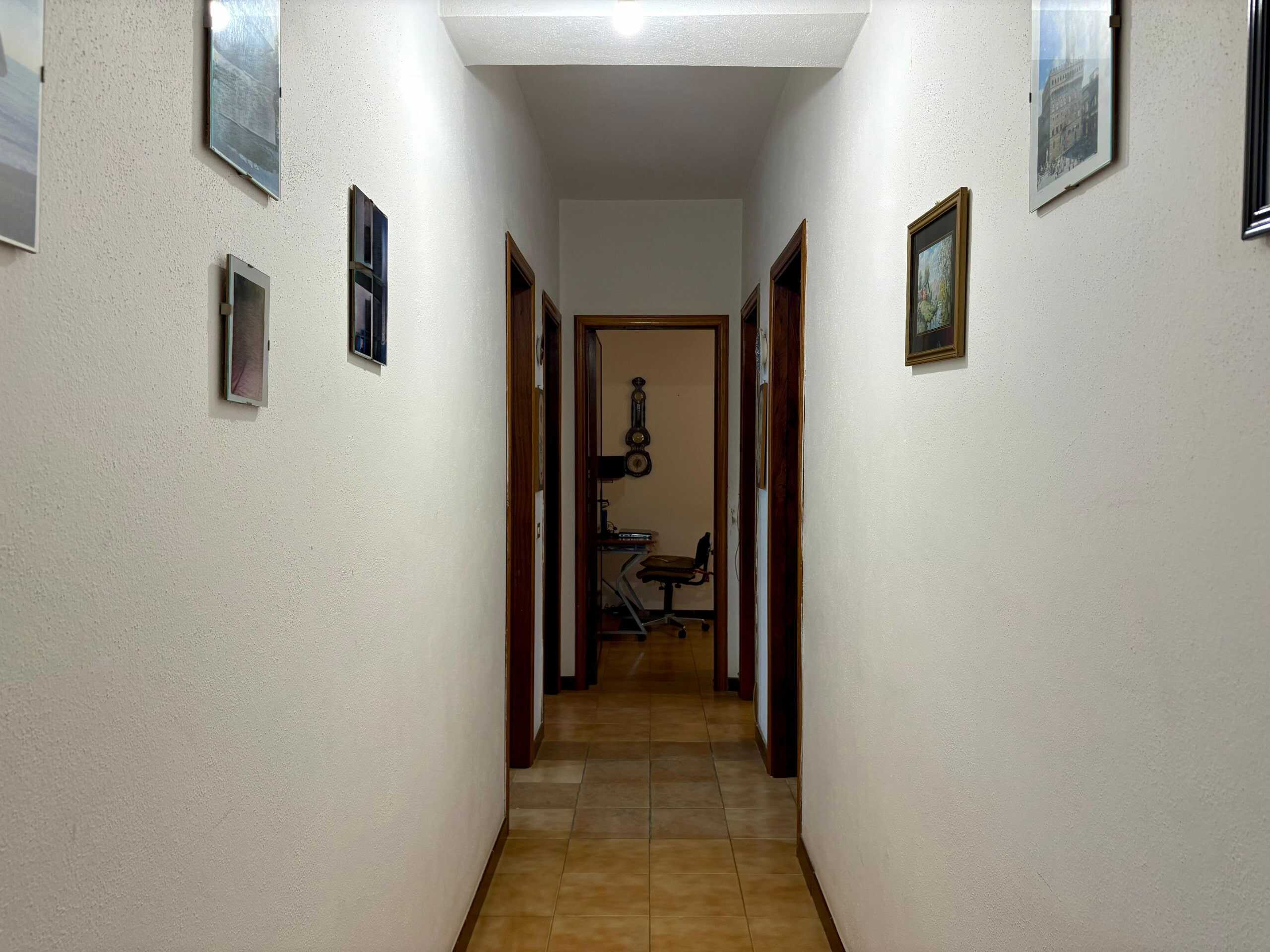 Corridor con pareti bianche e quadri appesi, vista verso una stanza con scrivania e sedia, pavimento in gres beige, atmosfera accogliente e ordinata, ideale per ambienti di casa o ufficio.