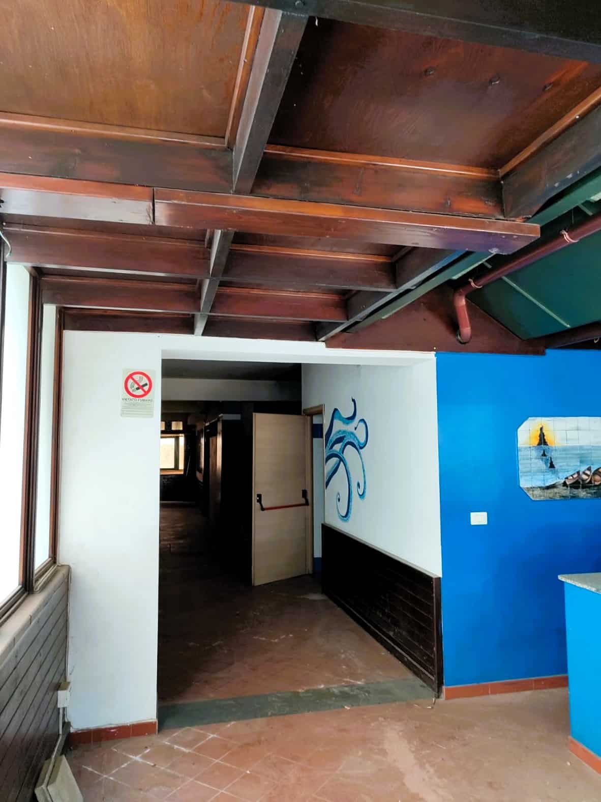 Tavolato di legno chiaro nel ristorante, pareti bianche, dettagli di decoro marino e affaccio su un'area interna con pavimento in piastrelle di terracotta.