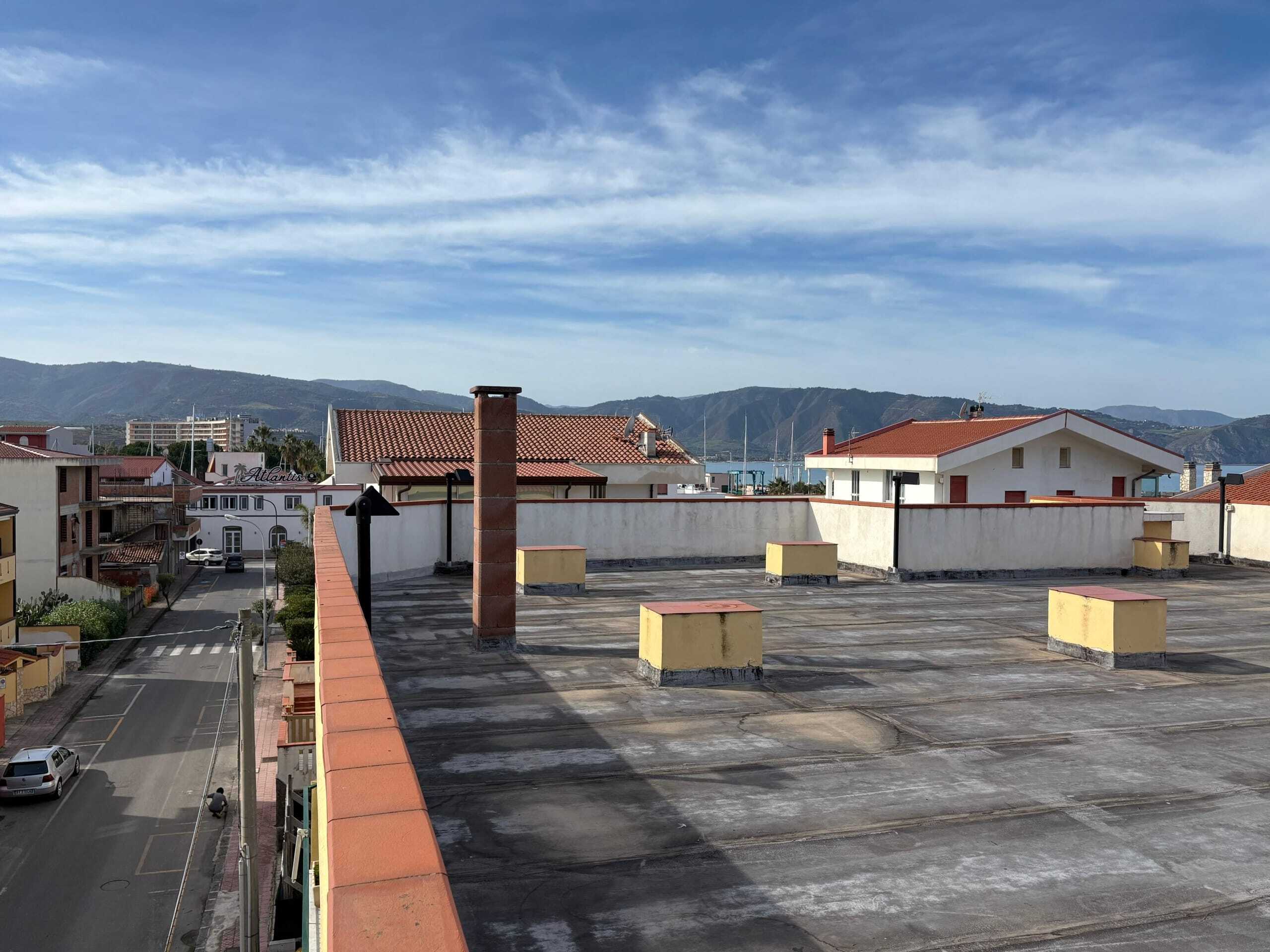 Ampio terrazzo sul tetto di un edificio residenziale con vista sui tetti delle case e sulle montagne sullo sfondo, ideale per la realizzazione di spazi esterni o solarium.