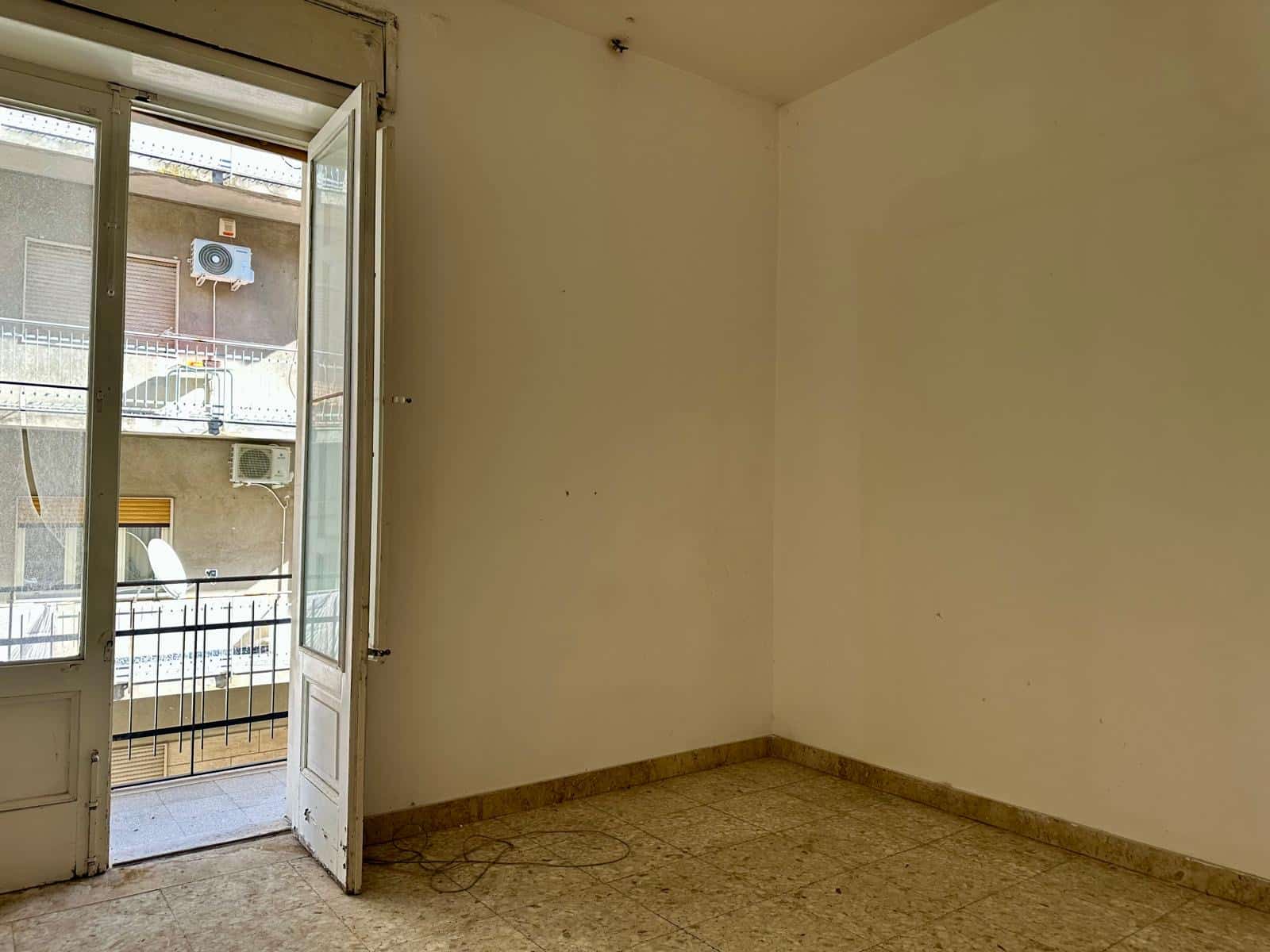 Balcone con porta finestra e vista su edifici circostanti, soggiorno spazioso da ristrutturare, ambienti luminosi per appartamenti in vendita a NextCasa.