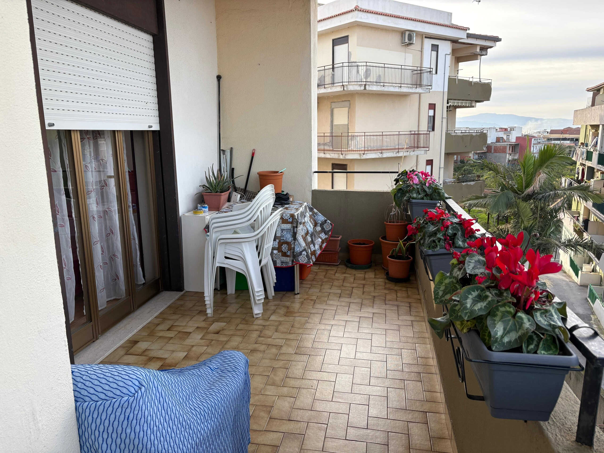 Balcone arredato con piante e sedie, vista su condomini e montagne, ideale per relax e giardinaggio.