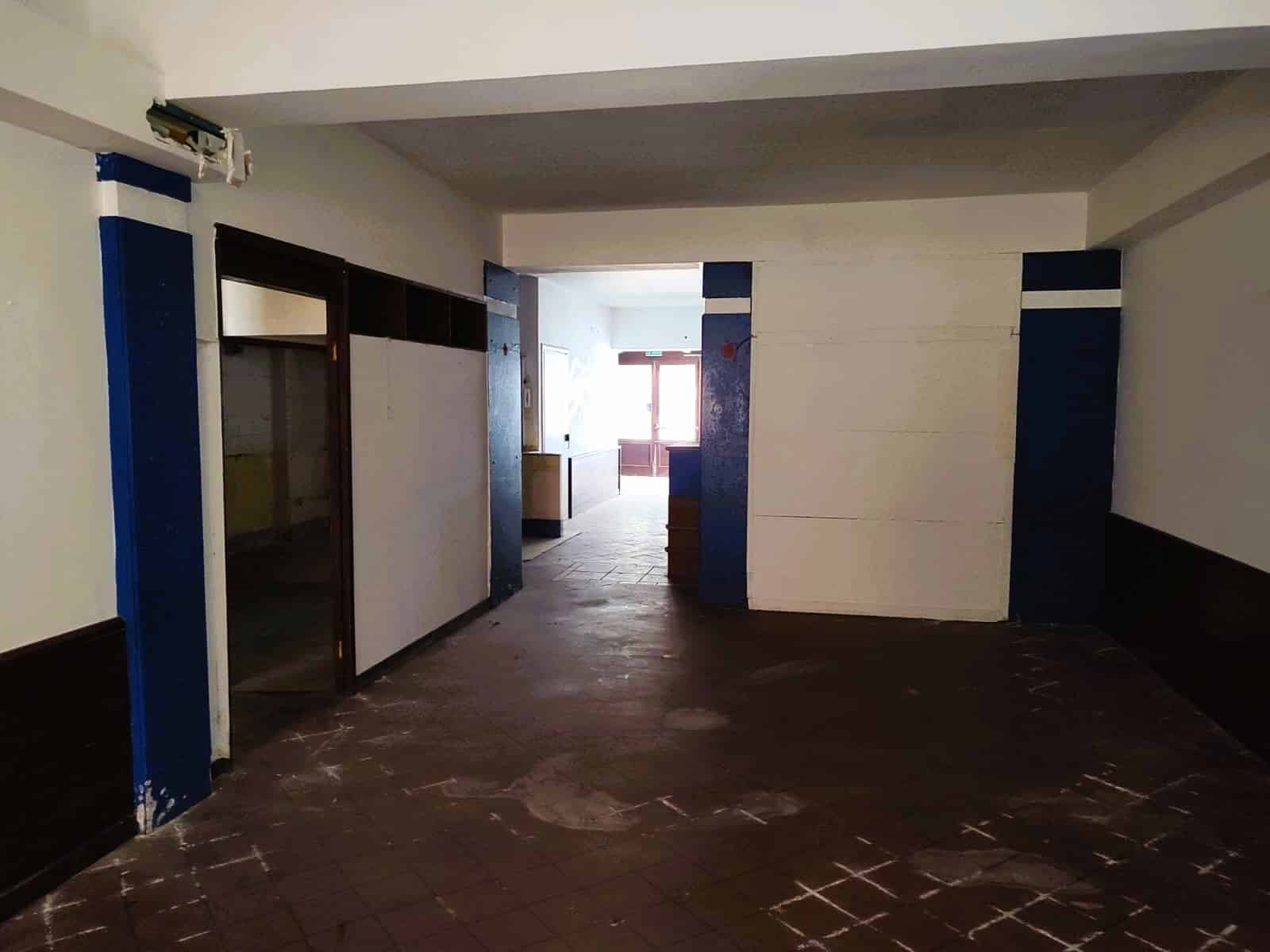 Ingresso di un appartamento in fase di ristrutturazione, con pareti dipinte in bianco e dettagli blu, pavimento in piastrelle di ceramica e luce naturale proveniente dalla finestra del soggiorno.