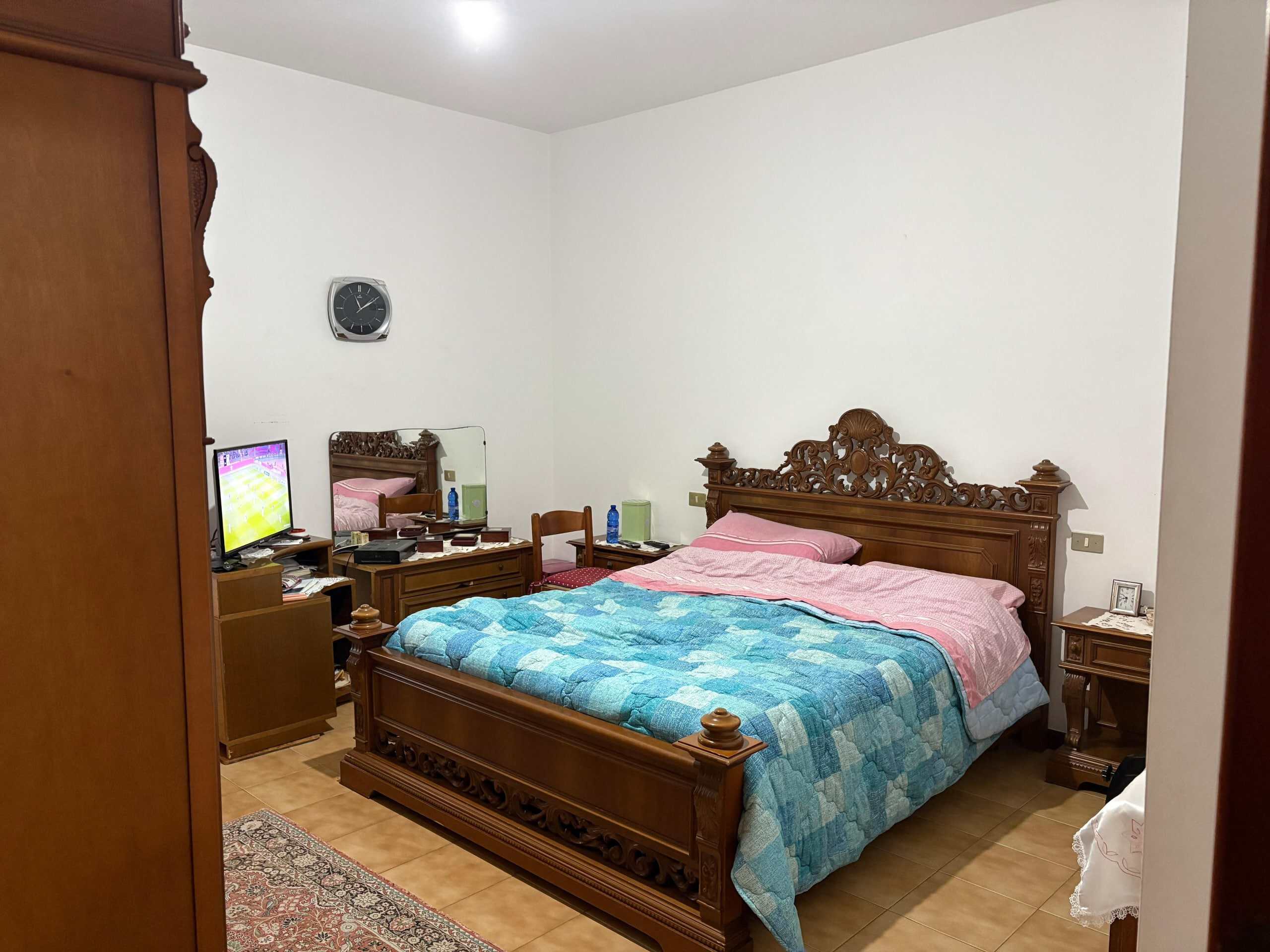 Letto matrimoniale in stile classico con intagliata testiera in legno, camera da letto arredata con mobili in legno scuro, ambiente accogliente e tradizionale.