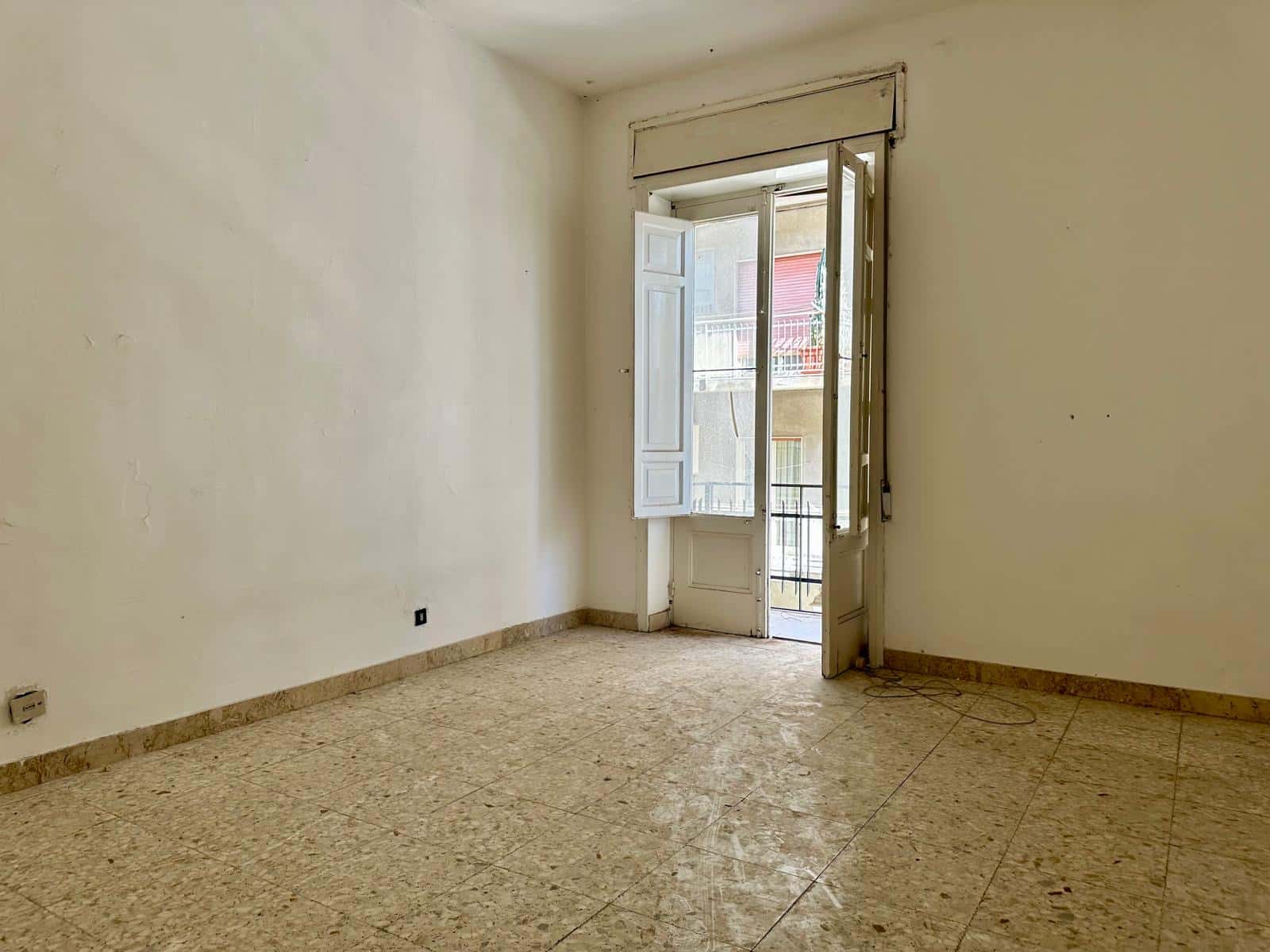 Finestra luminosa e balcone in un appartamento vuoto con pareti bianche e pavimento in marmo beige, ambiente spazioso pronto per essere arredato e personalizzato.