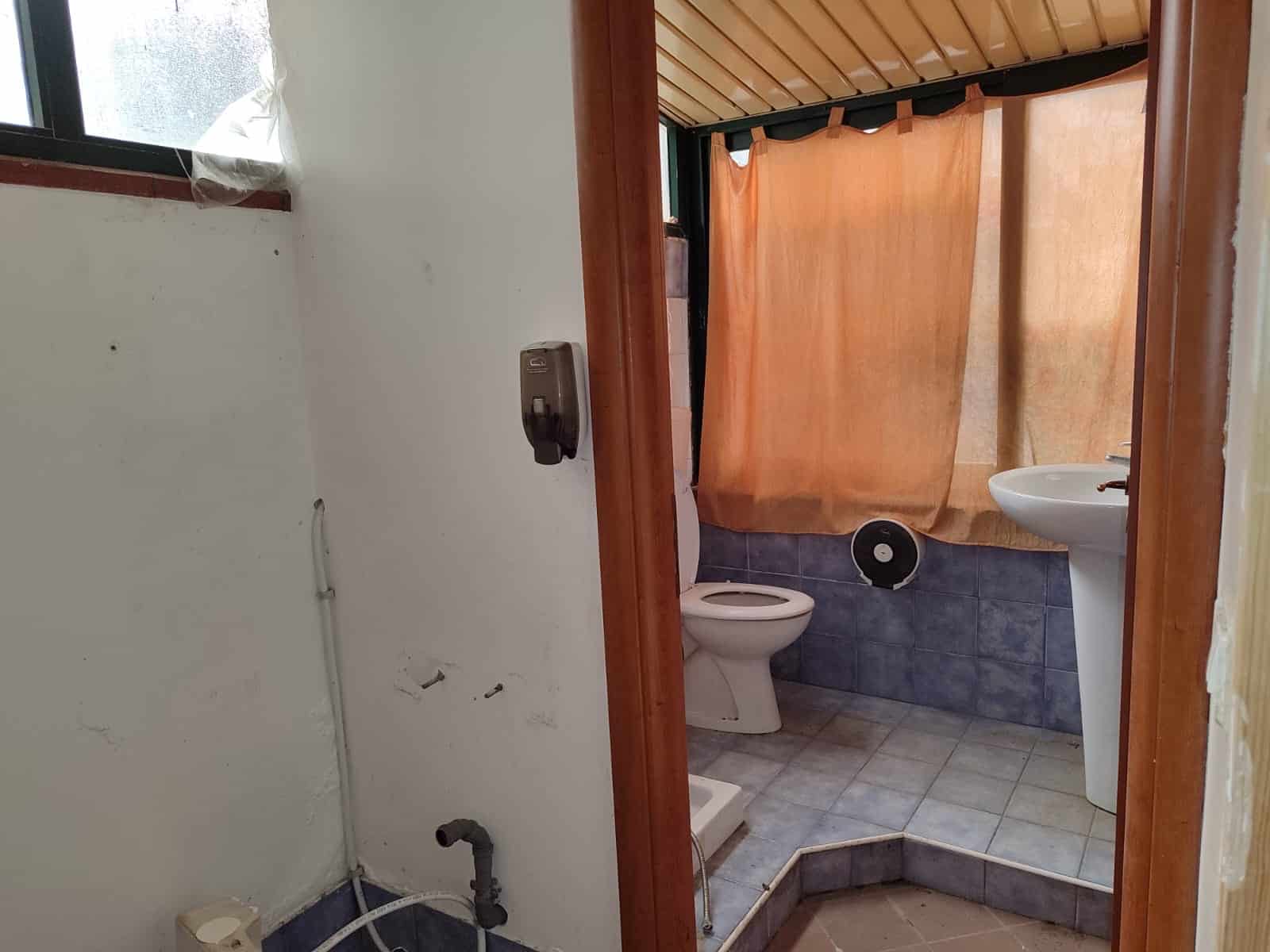 Bagno in fase di ristrutturazione con pareti in piastrelle blu, tenda arancione e lavabo con water, spazio compatto e funzionale, ideale per case e appartamenti in vendita o affitto.