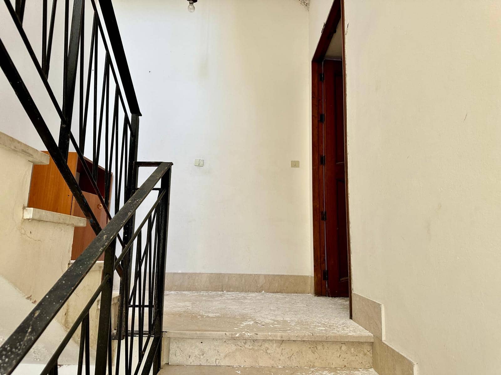 Scalinata in interior di casa in fase di ristrutturazione, con ringhiera in ferro nero e pareti bianche.