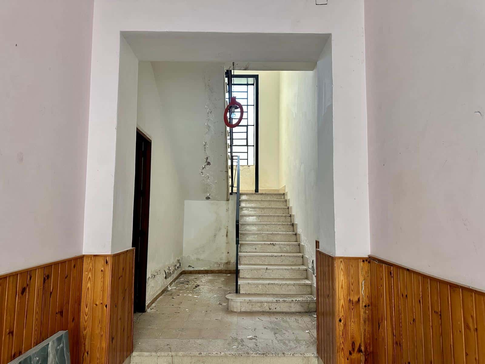 Scala in cemento con ringhiera metallica per l'accesso al piano superiore in un edificio in fase di ristrutturazione, con muri con evidenti segni di sgretolamento, in un ambiente interno.