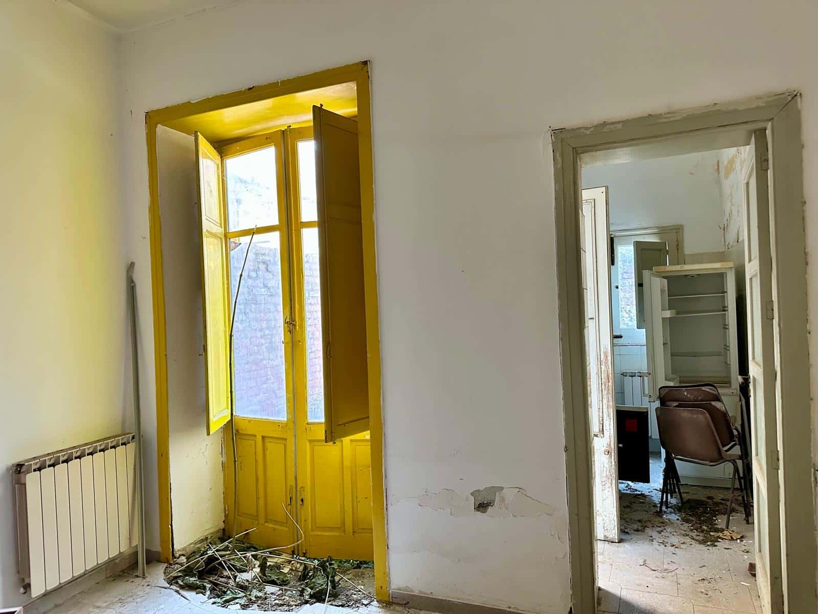 Finestra con infissi gialli in una stanza abbandonata, facente parte di un immobile da ristrutturare, che mostra segni di degrado e disordine.