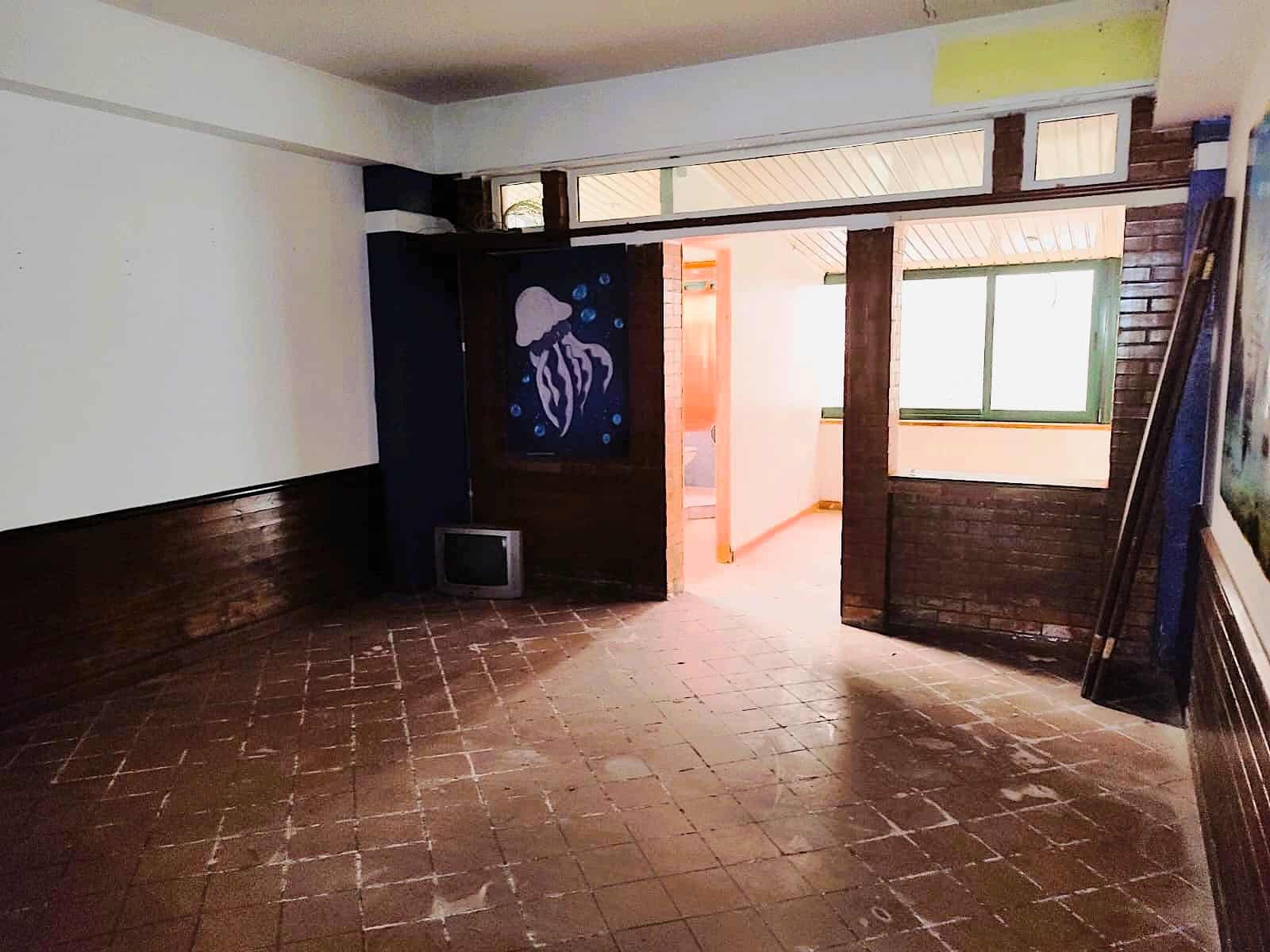 Spazio interno di un immobile con pareti in mattoni a vista, grande finestra e pavimento in piastrelle rosse, ideale per progetti di ristrutturazione e interior design.