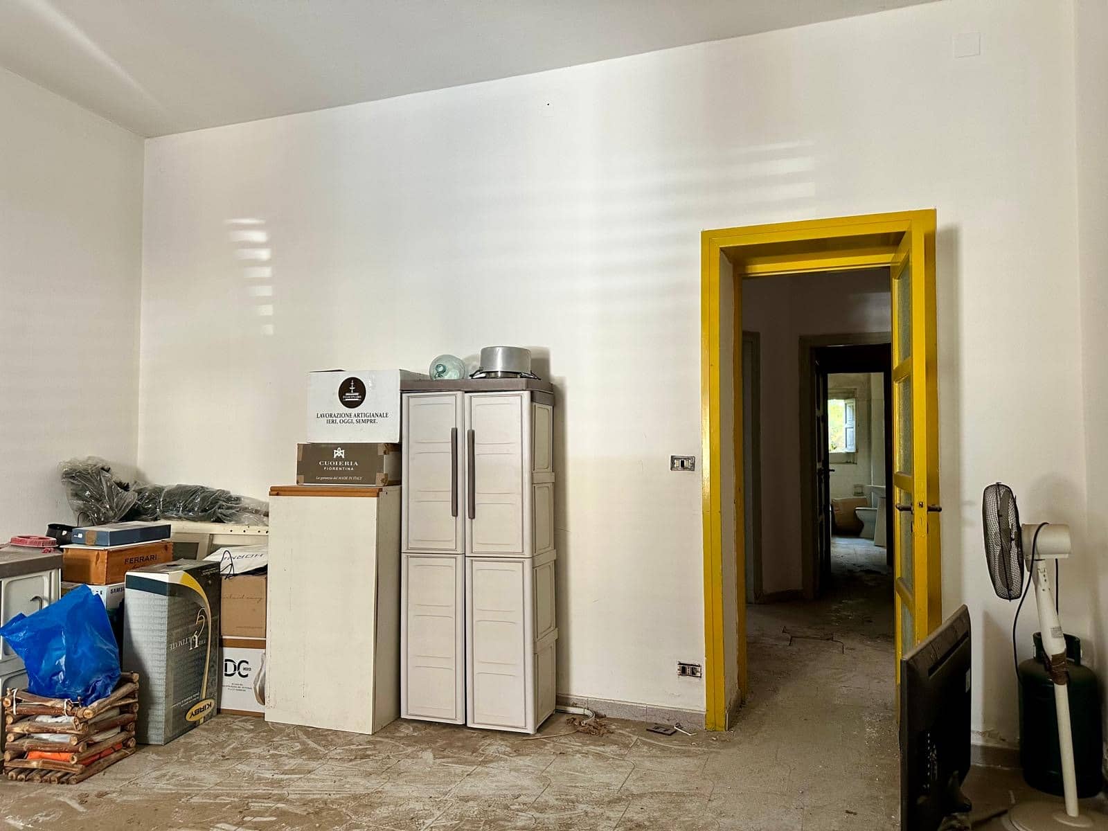 Vestibolo di casa in fase di ristrutturazione, con porta in legno giallo, oggetti di immagazzinamento, scatole e utensili, pavimento in piastrelle e pareti bianche, pronta per essere arredato e personalizzato.
