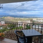 Vista panoramica mare e colline da terrazza con balcone in stile rustico, arredato con tavolo e sedie, su sfondo di cielo nuvoloso, suggestivo scenario di appartamento NextCasa Italia.