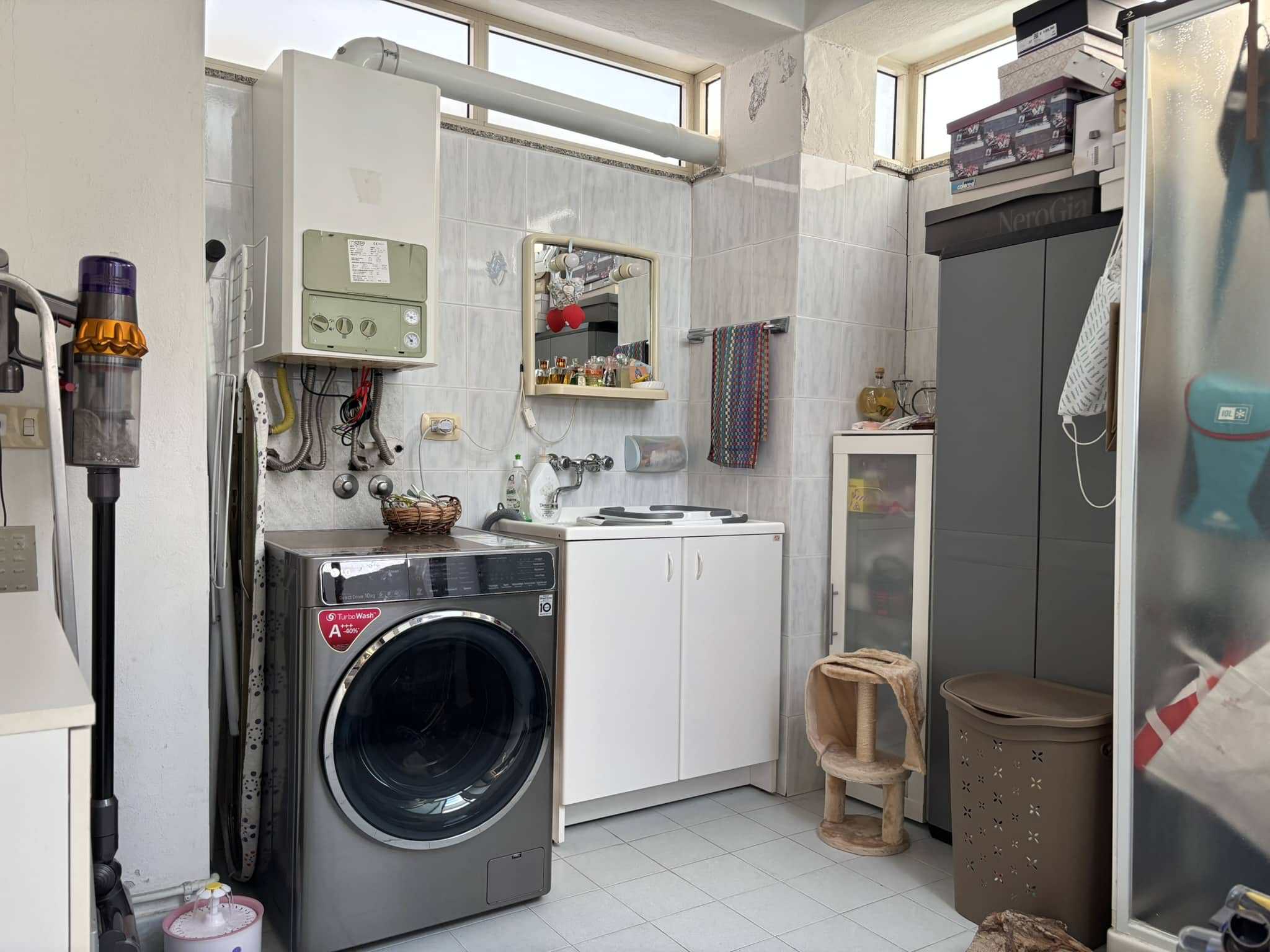 Lavanderia compatta con lavatrice, armadi e spazio per oggetti domestici, illuminata da finestra alta, ideale per servizi di casa e organizzazione degli spazi abitativi.