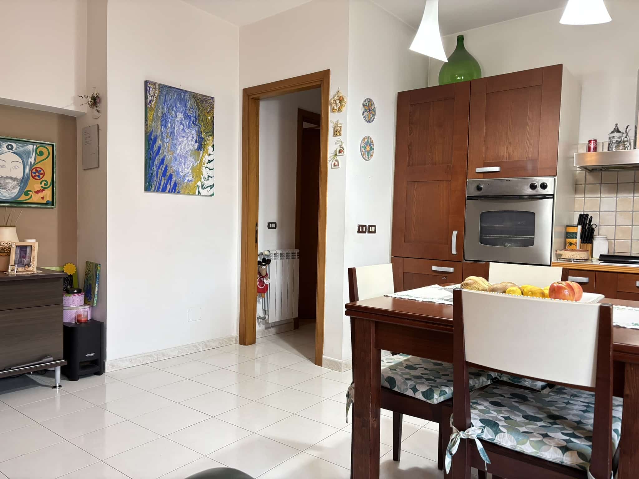 Ampia cucina moderna con mobili in legno, tavolo da pranzo e elettrodomestici integrati, pareti decorate con quadri colorati, ambiente luminoso e accogliente, perfetto per vivere e cucinare con stile.