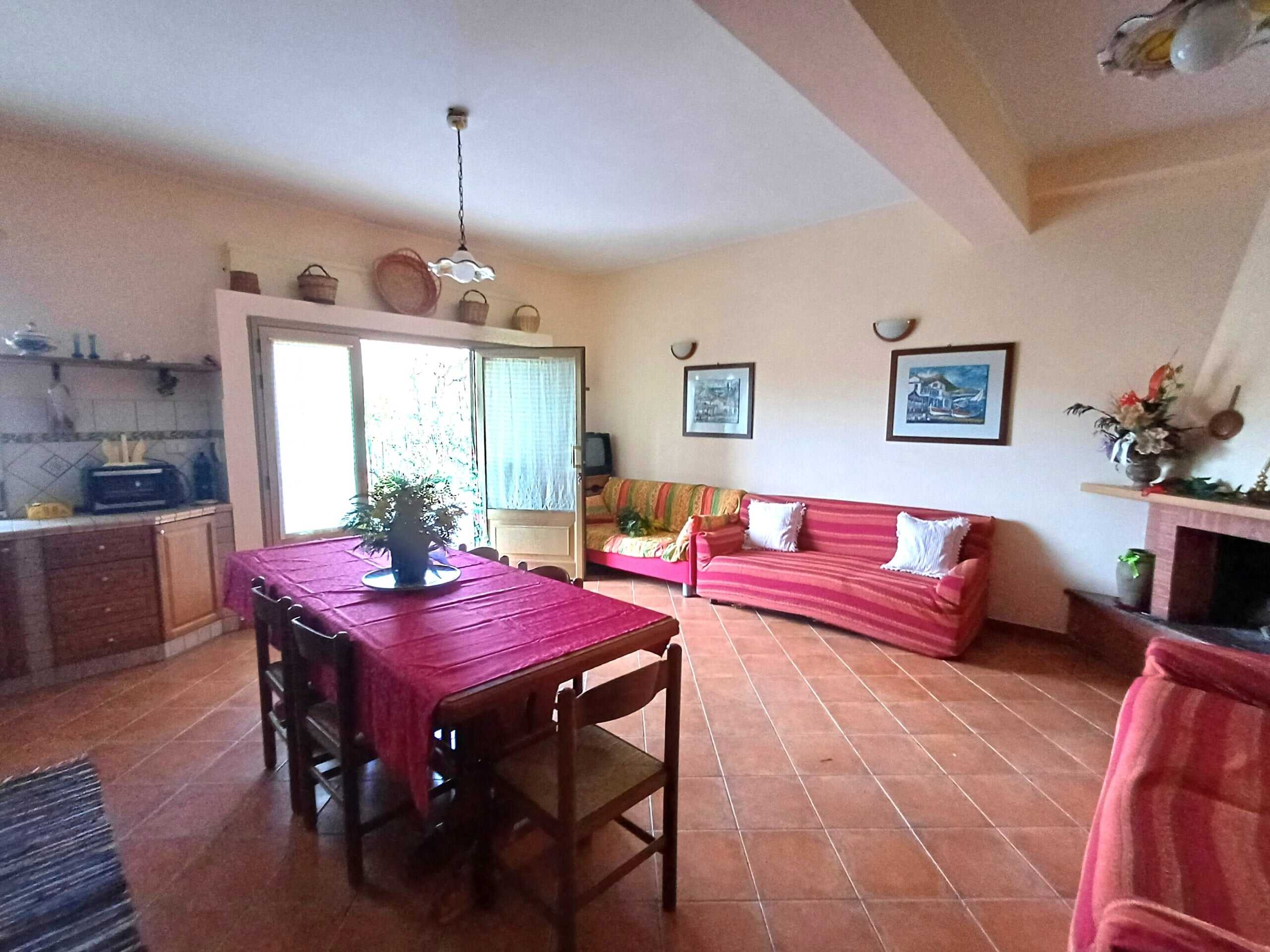 Sedie in legno, soggiorno con divani rossi, pareti color crema, camino e tavolo apparecchiato con piante e decorazioni.