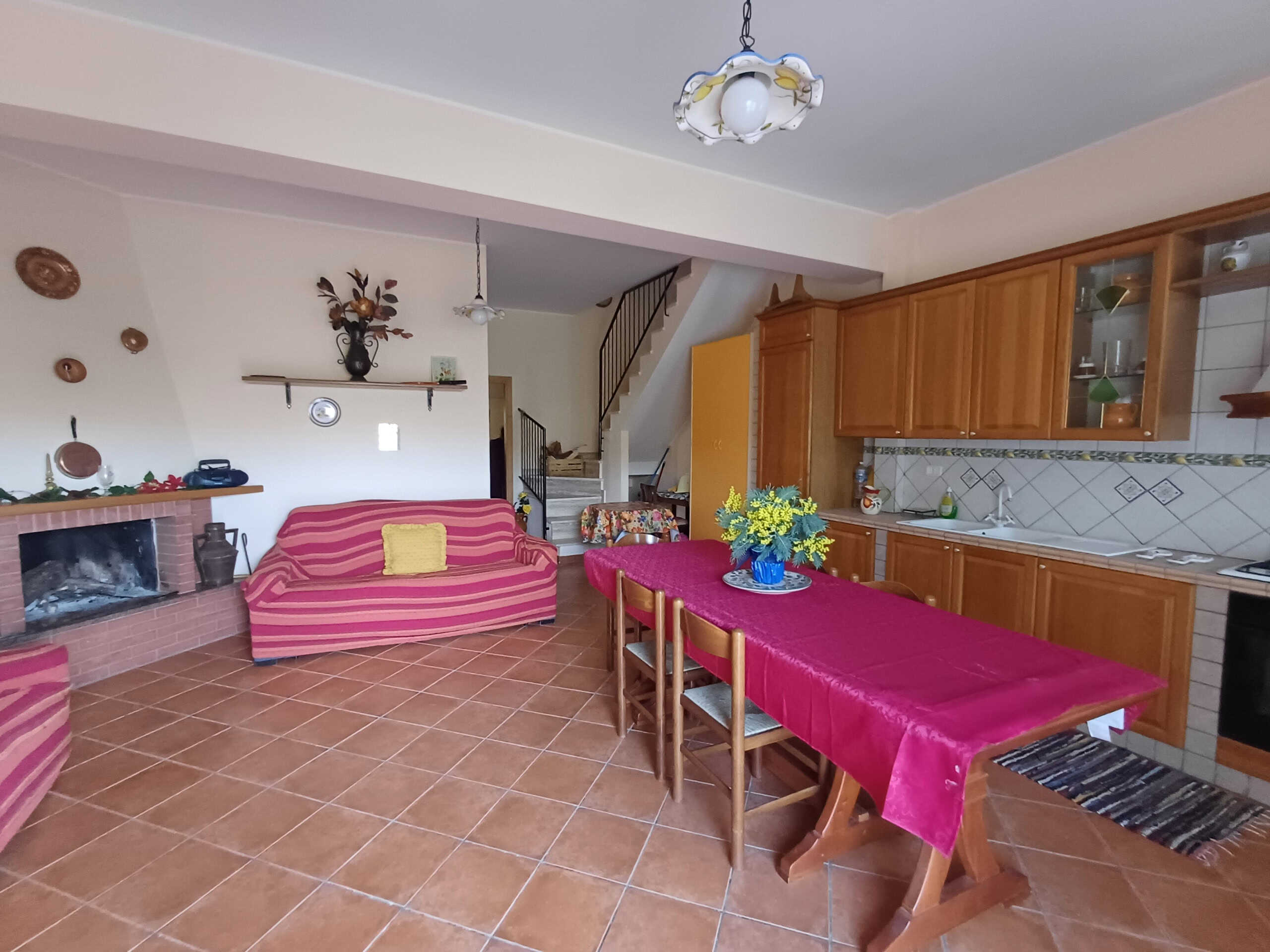Accogliente soggiorno con camino e zona pranzo in stile rustico, arredato con mobili in legno e tessuti colorati, ideale per vivere momenti di relax e convivialità.