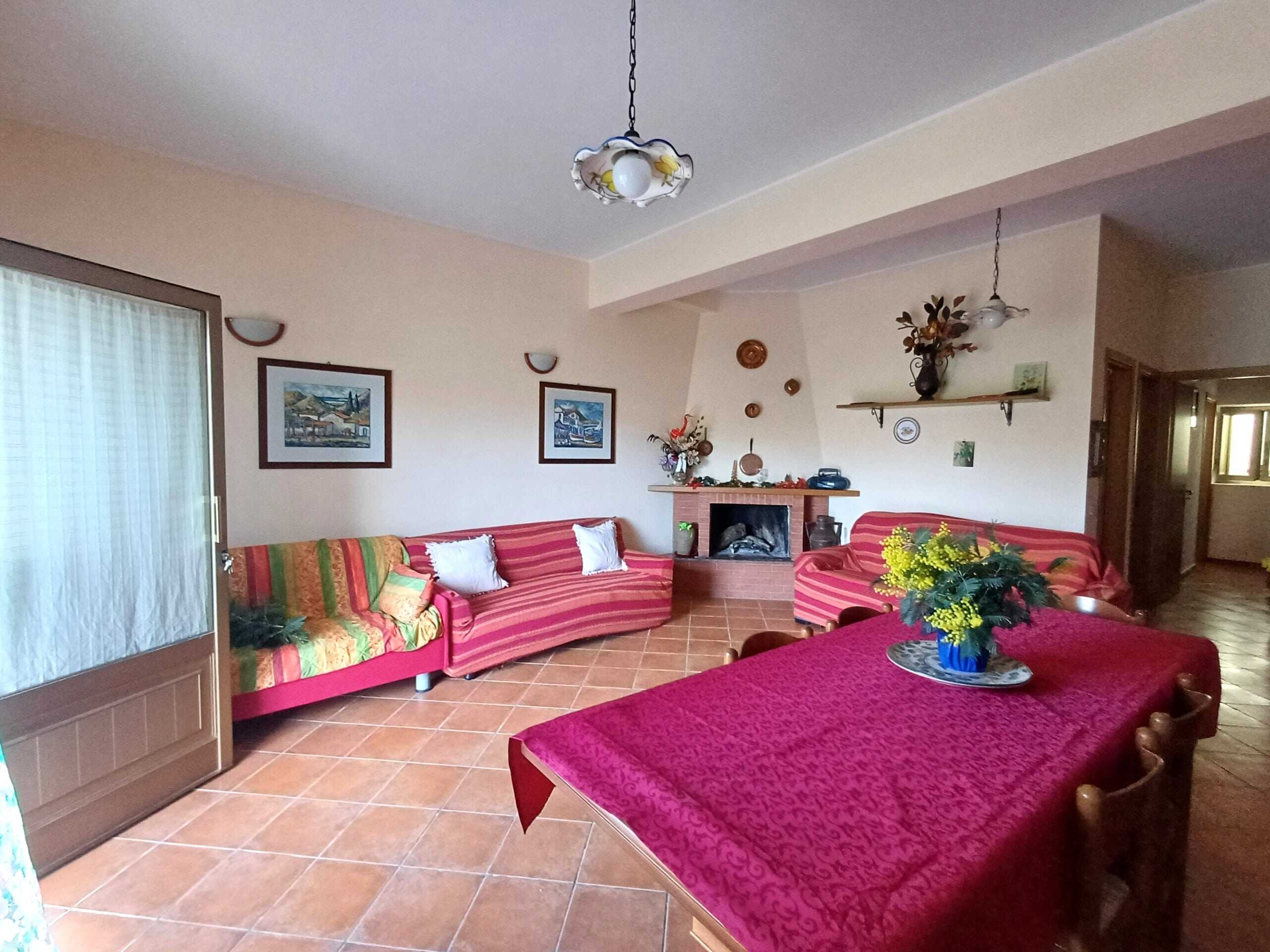 Soggiorno con divani colorati, camino in muratura, tavolo con tovaglia rossa e decorazioni vintage, atmosfera accogliente e classica adatta a case di charme.