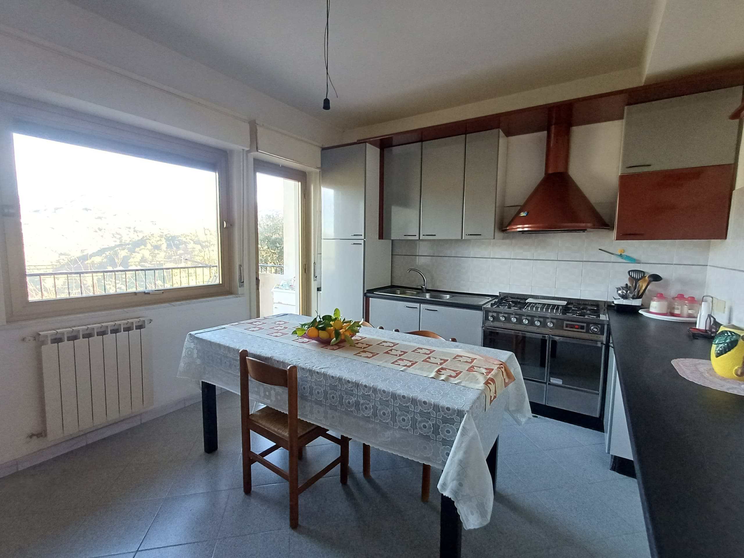 Elegante cucina abitabile arredata con moderni mobili, ampia finestra con vista panoramica, piano cottura a gas, tavolo per pranzi e colazioni, atmosfera luminosa e accogliente.