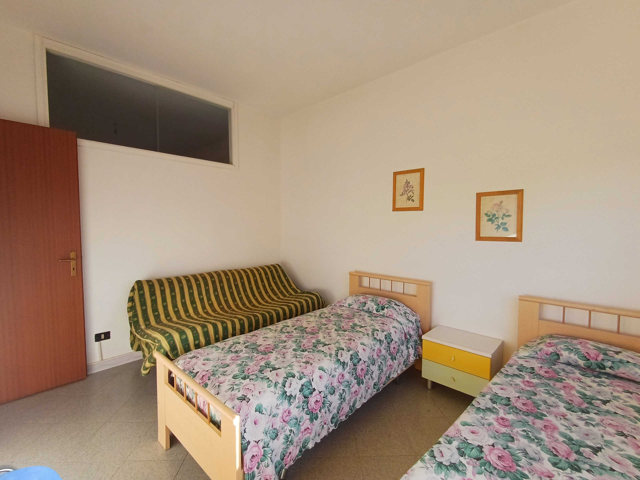 Dormitorio con due letti singoli, letto matrimoniale e divano letto, arredamento semplice, pareti bianche e decorazioni floreali, ideale per soggiorni in famiglia o amici.