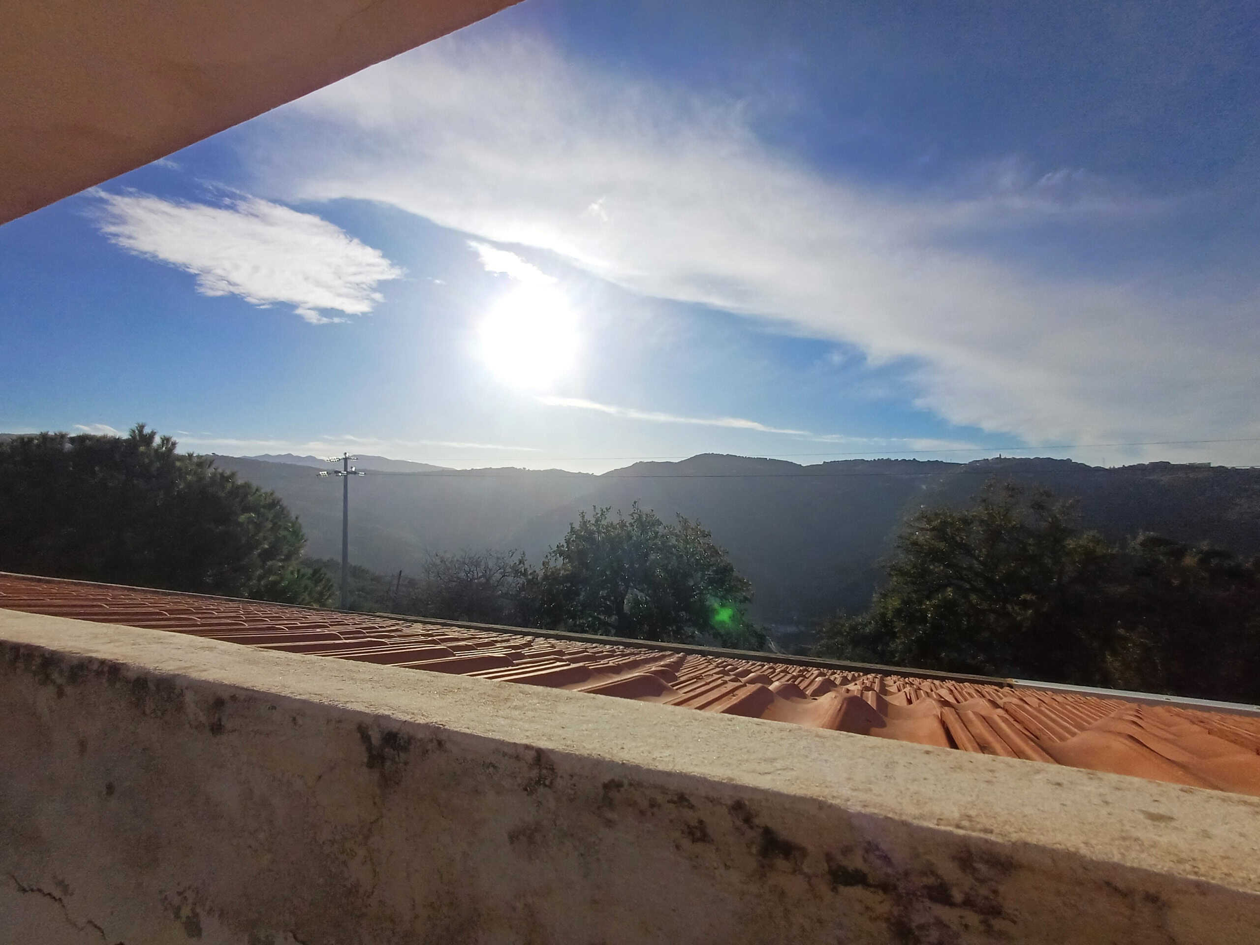Luminoso panorama di montagna al tramonto visto da un balcone soleggiato con tetto in terracotta e cielo azzurro, ideale per case vicine alla natura.