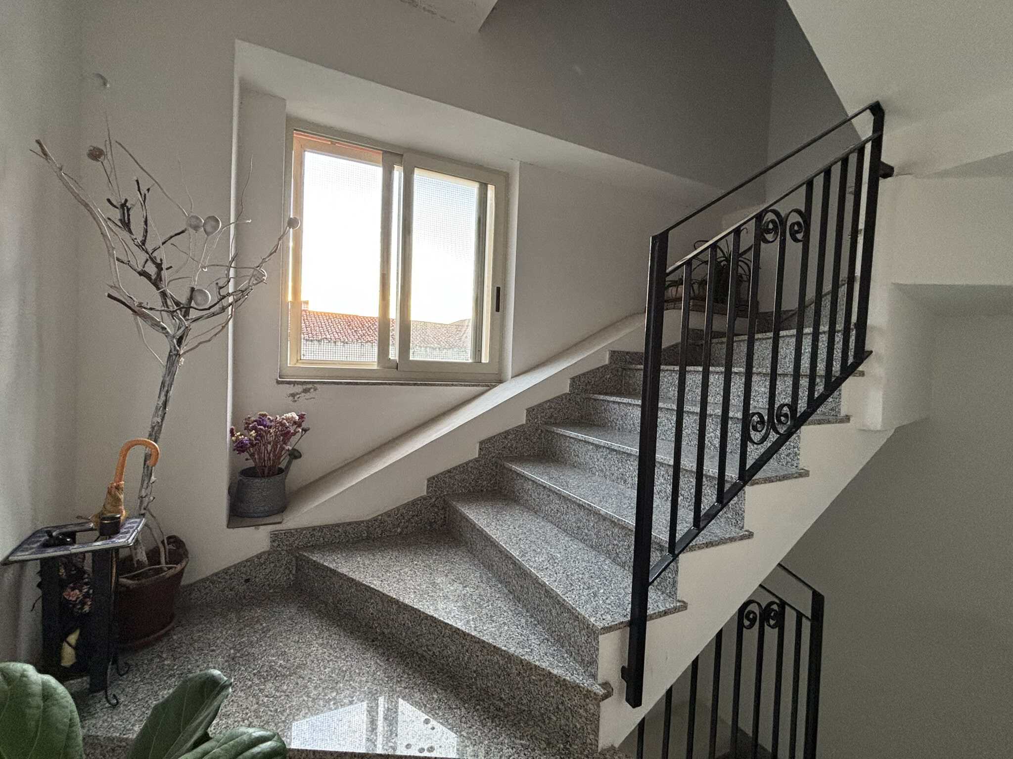 Scala interna in granito con ringhiera in ferro battuto, luce naturale, arredo semplice, adatta a case di città o appartamenti moderni.