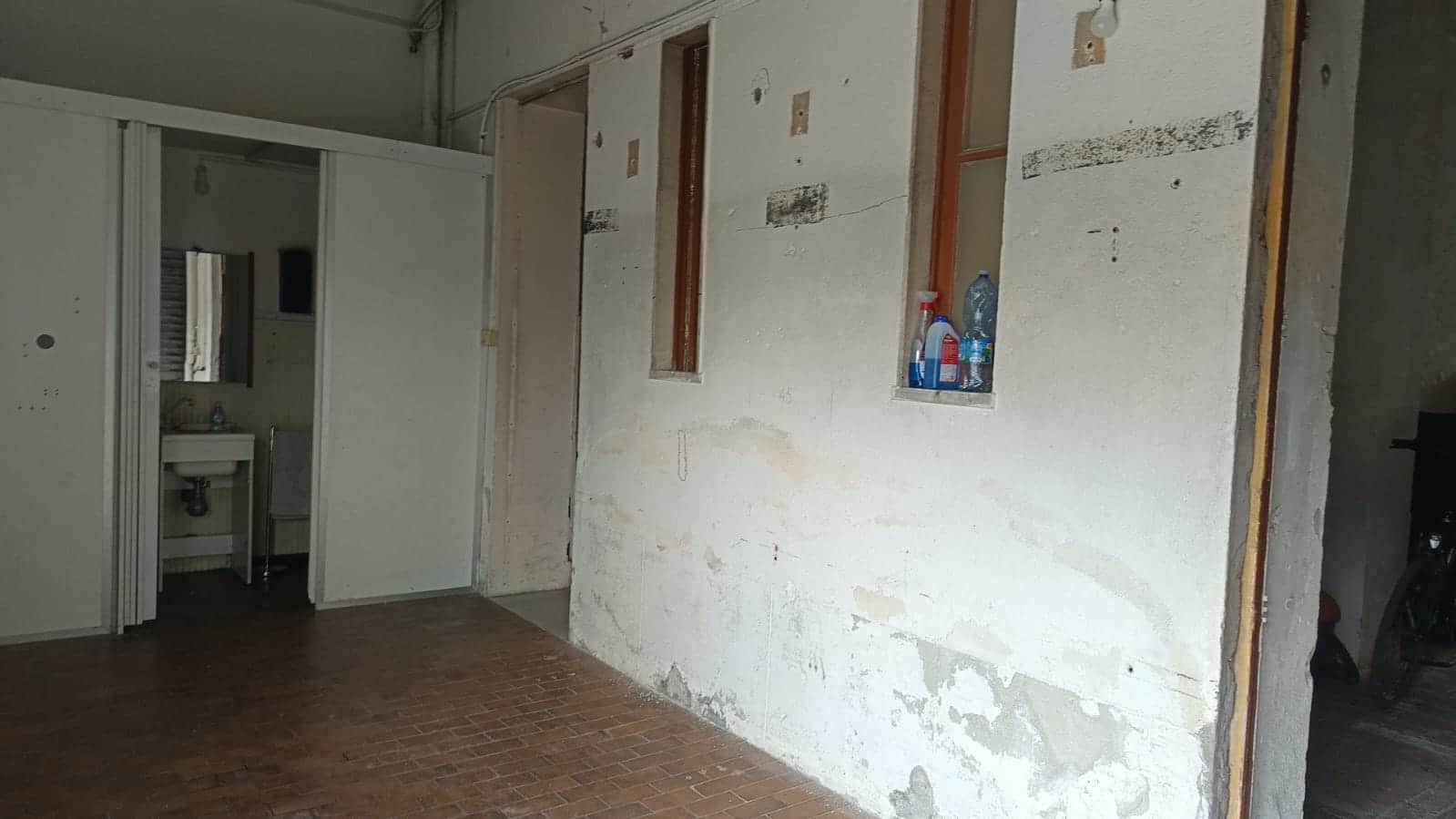 Altezza di una parete in fase di ristrutturazione con nicchie e tubature, pavimento in cotto e ambiente di progetto.