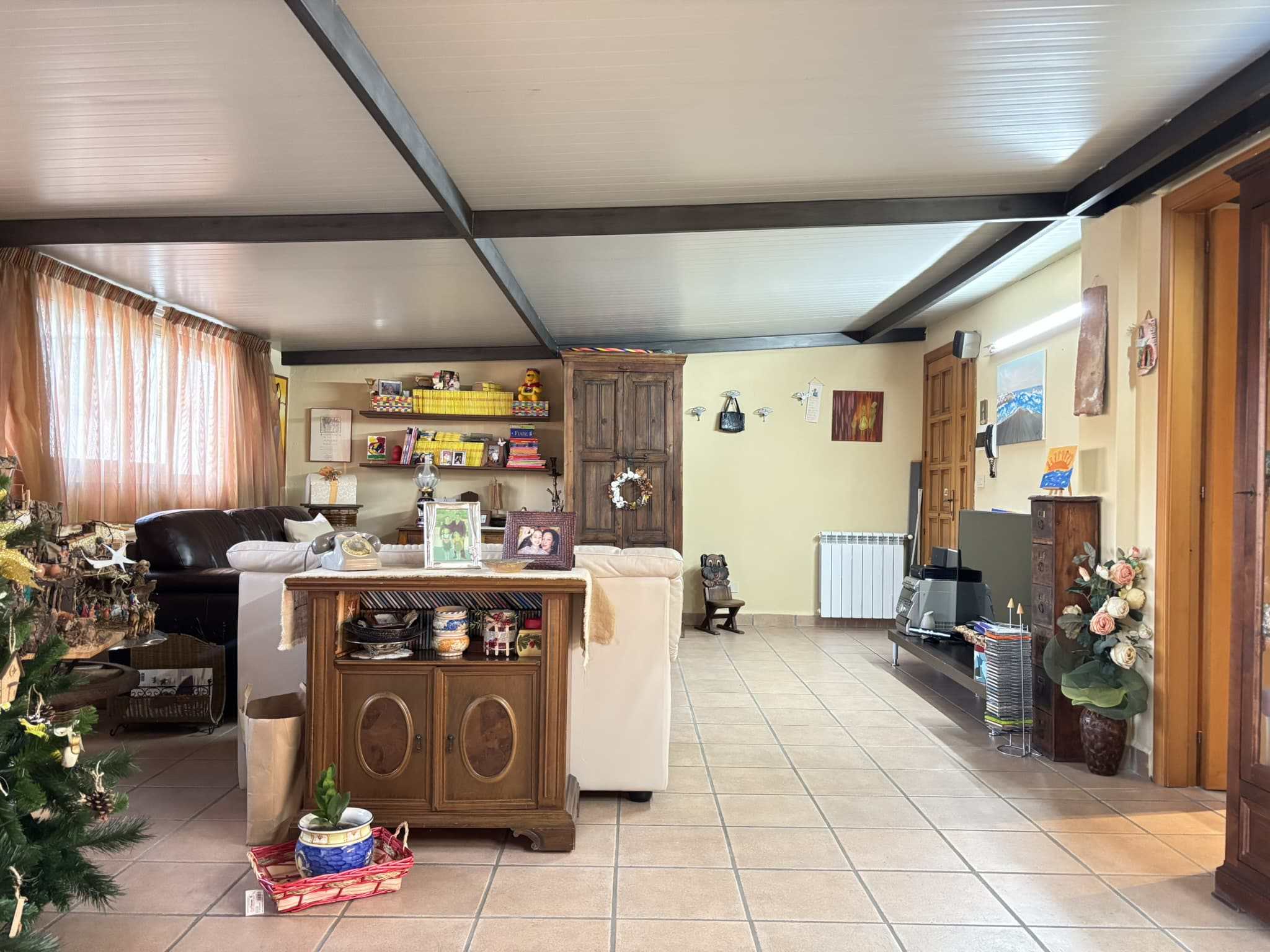 Immagine di un soggiorno spazioso e accogliente con arredamento classic, divani, mensole con libri, decorazioni natalizie, amplia finestra con tende leggere, pavimento in piastrelle e dettagli di design rustico.