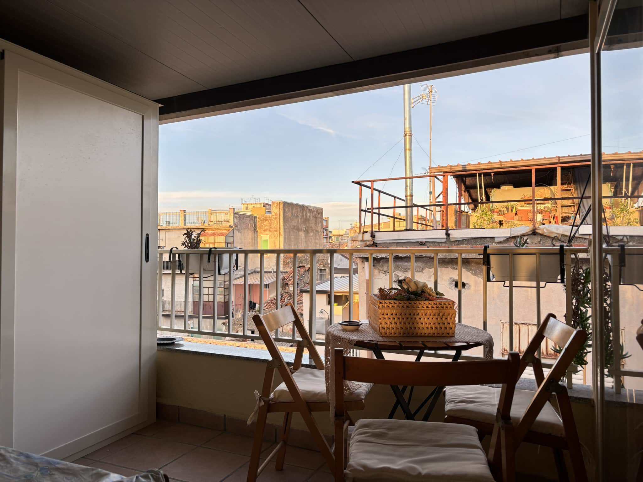 Balcone di un appartamento con vista sulla città, arredato con tavolo e sedie per pranzi all'aperto, illuminato dal tramonto, stile accogliente e moderno.