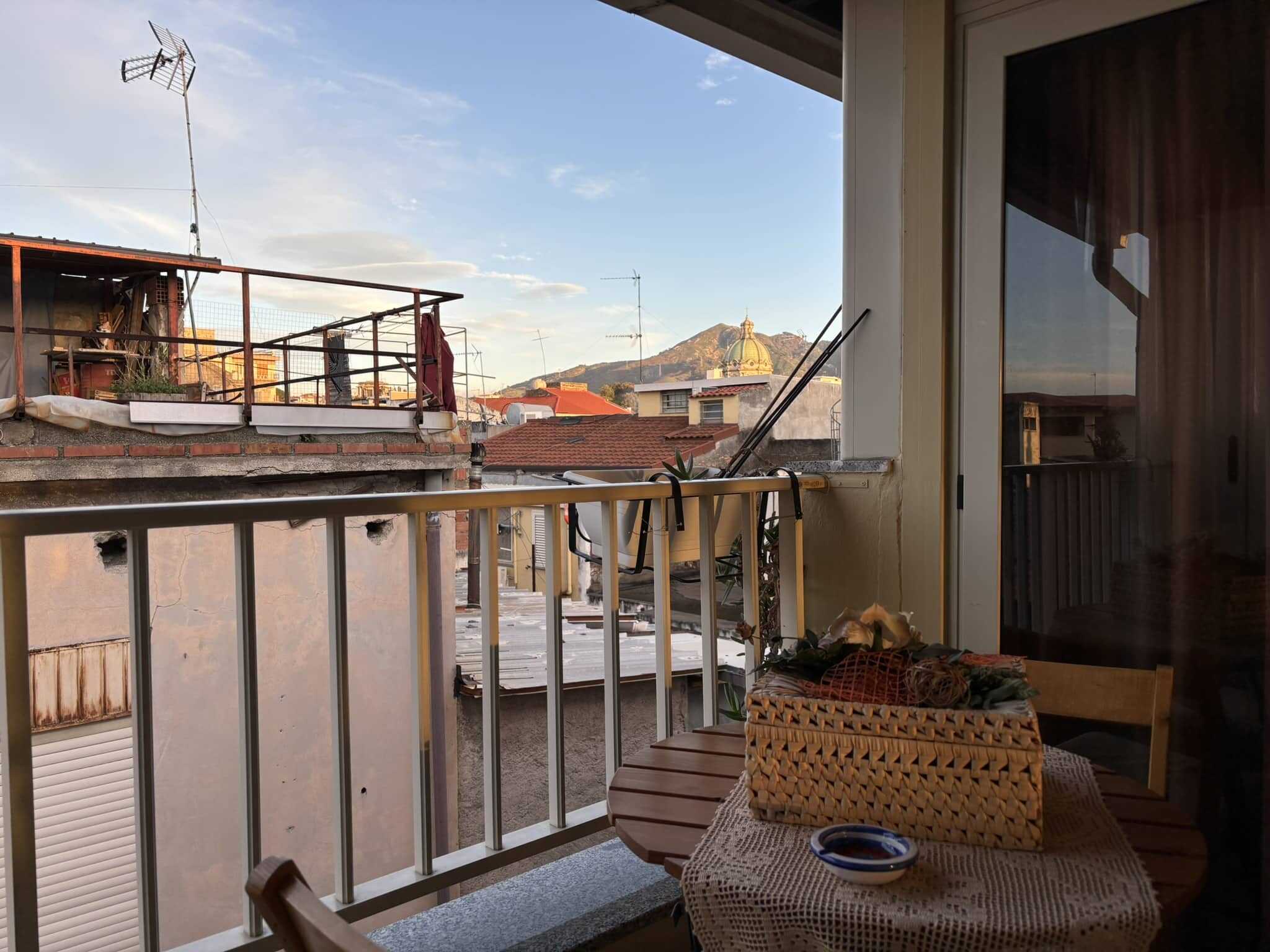 Balcone soleggiato con vista sulla città e sui monti, arredato con piante e oggetti decorativi, ideale per vivere momenti di relax all'aperto nel centro di Napoli.