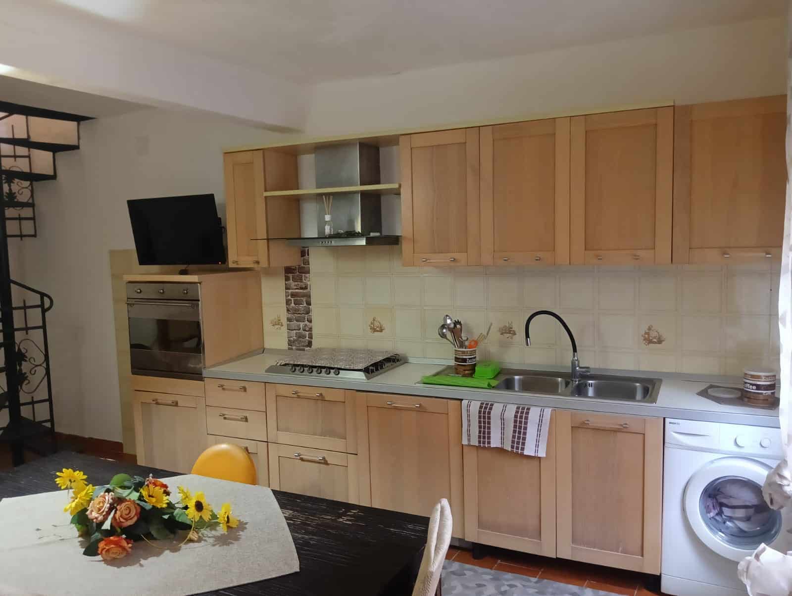 Cucina moderna in stile classico con mobili in legno chiaro, piano di lavoro in laminato e elettrodomestici integrati, ideale per appartamenti e case con arredo pratico e funzionale.
