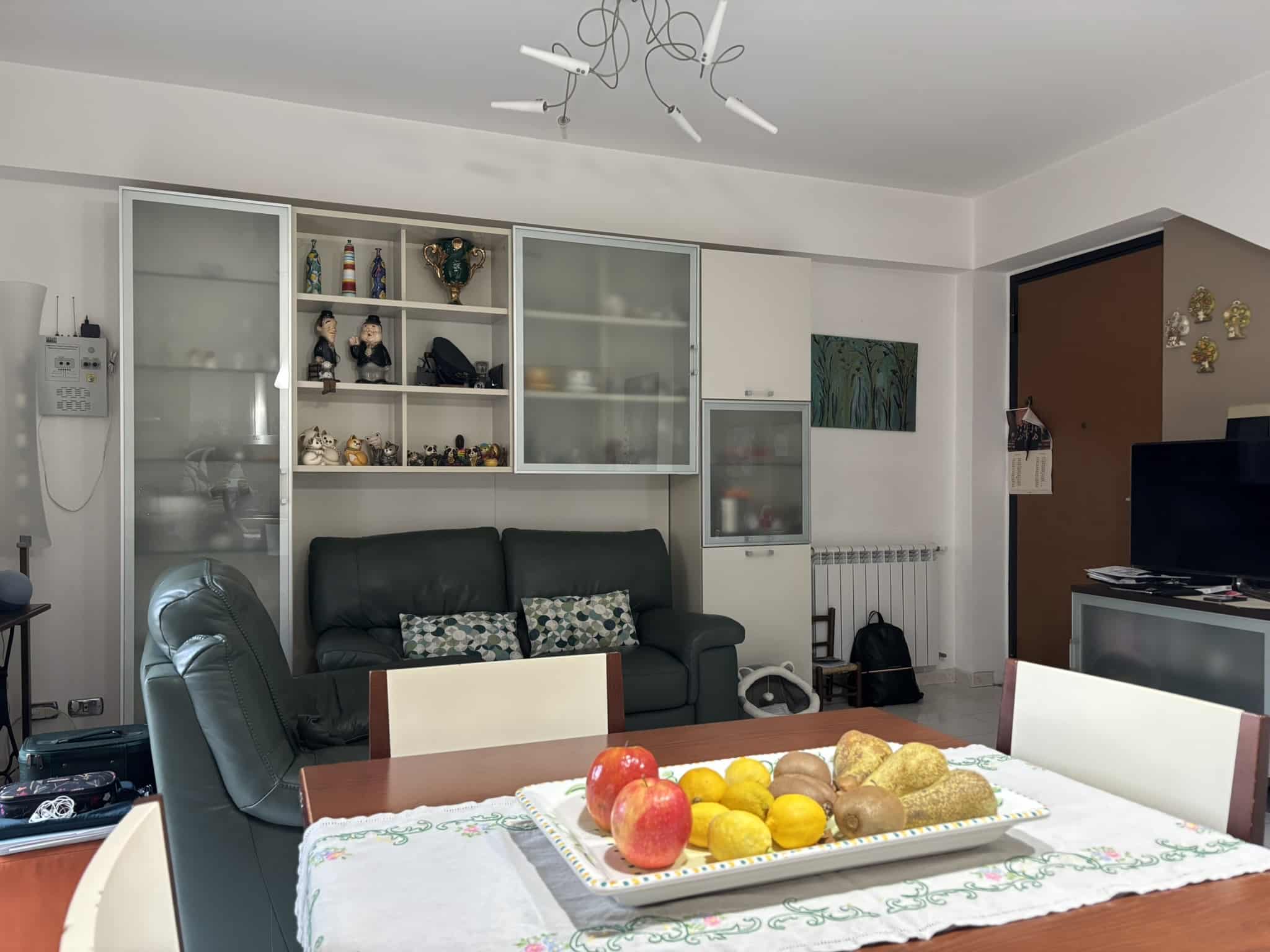 Pompeia casa con soggiorno moderno, pareti bianche, divano in pelle e tavolo da pranzo con frutta fresca, decorazioni e televisore, ambiente accogliente e arredato con stile, ideale per vivere comodamente.