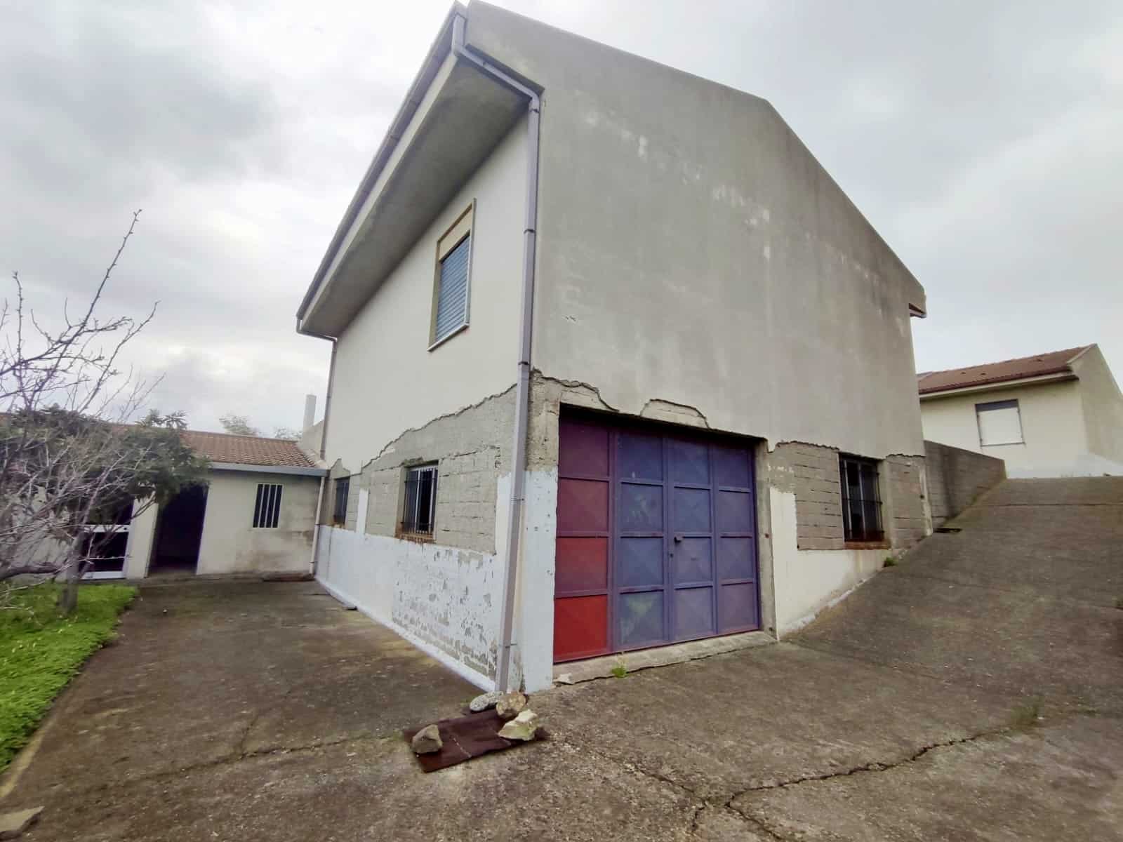 Vecchio edificio residenziale con garage, pareti danneggiate e struttura in fase di ristrutturazione, in un contesto di abitazioni vicine.
