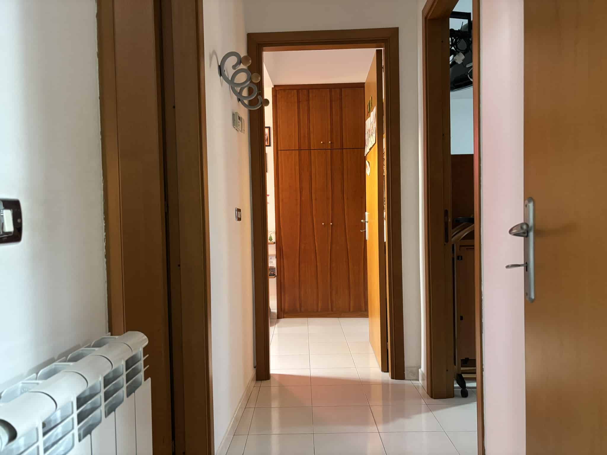 Porta di ingresso di un appartamento con porte in legno, vista di un corridoio con cucinino e armadio in legno, ambiente luminoso e ben organizzato, ideale per soluzioni di case e affitti.
