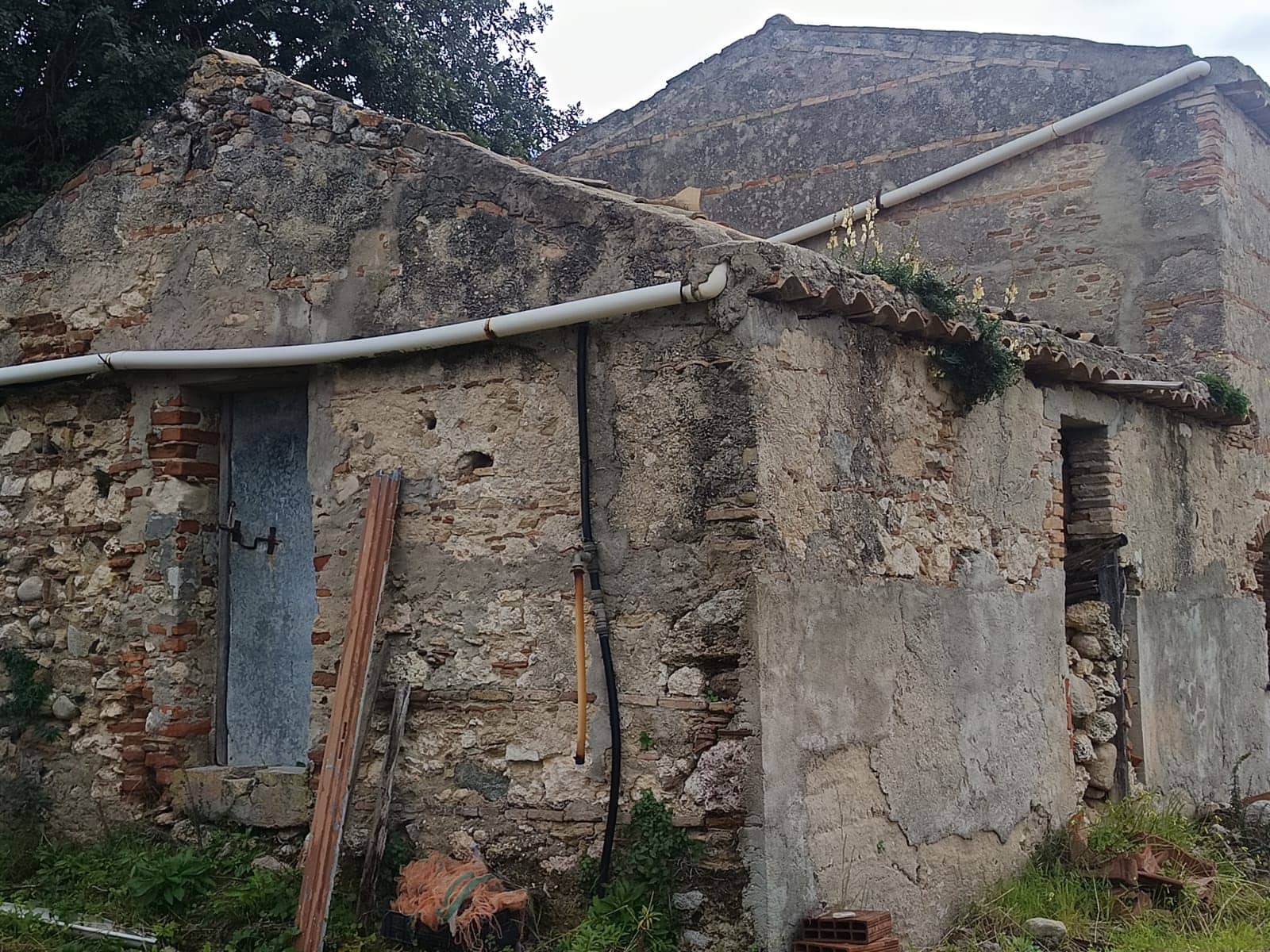 Vecchia casa in pietra ristrutturata, con carattere rustico e muri in pietra, ideale per ristrutturazione o restauro, situata in ambiente naturale e tranquillo, con tetto in tegole e tubature esterne visibili.