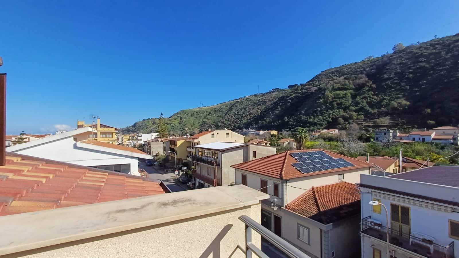 Tetto con pannelli solari elitarianici, vista sulla città e sulle colline verdi, case residenziali e paesaggi naturali, efficienza energetica, casa sostenibile, panorama urbano, energia solare, NextCasa.