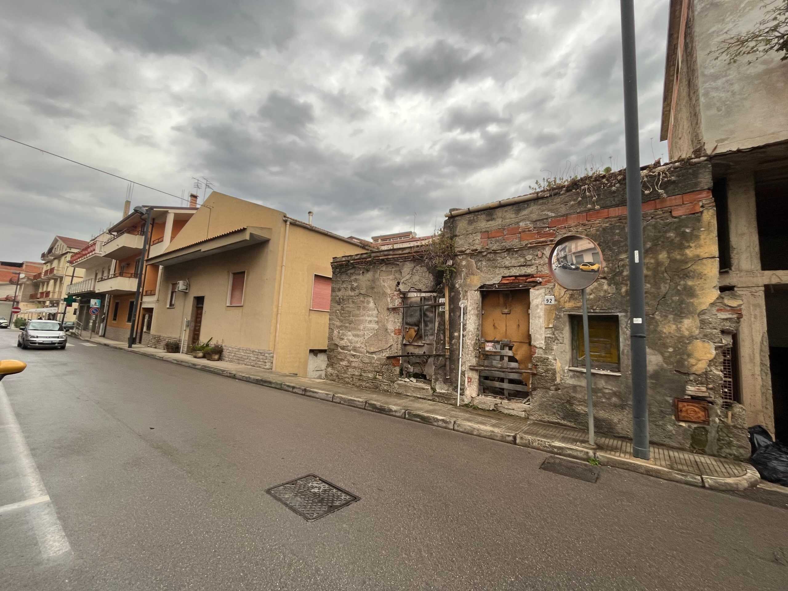 Vecchio edificio abbandonato in via urbana con mura in pietra e cartongesso, atmosfera nebbiosa e cielo nuvoloso.