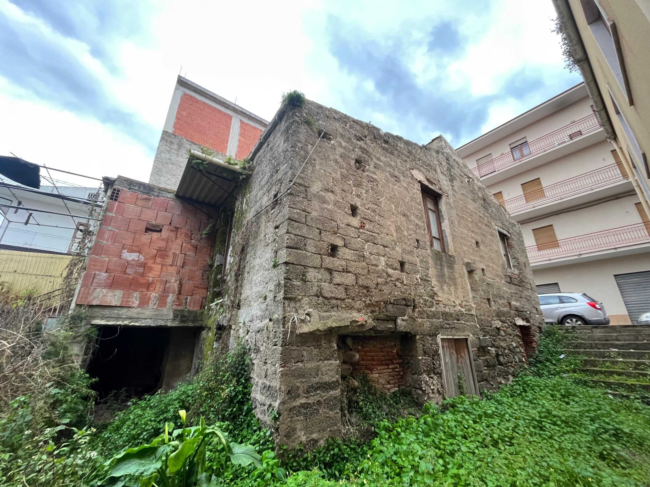 Vecchio edificio in pietra con superfici in mattoni rosso, situato in zona urbana con presenza di arredo moderno e veicoli parcheggiati; ideale per ristrutturazione o progetto di riqualificazione immobiliare.