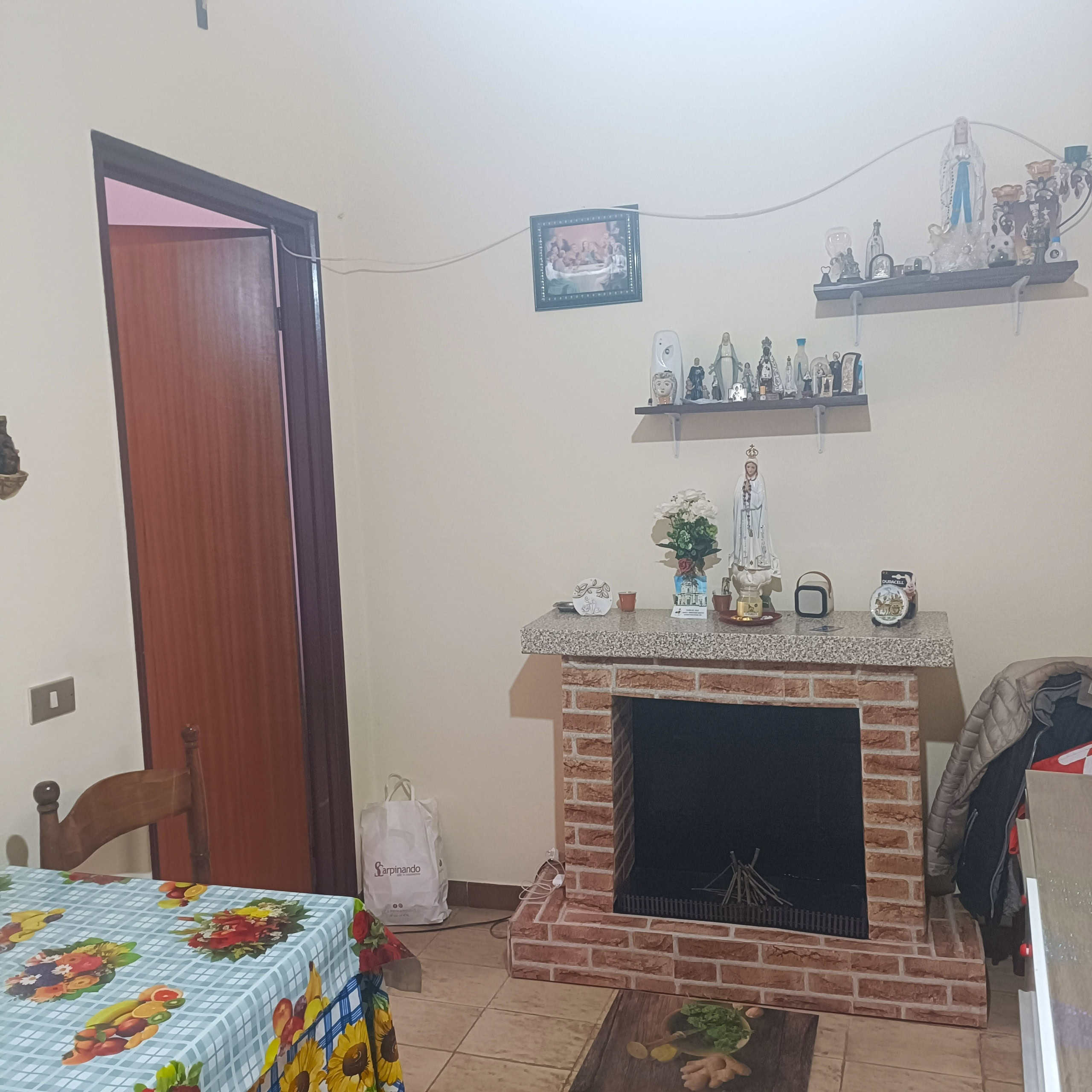 Moderno camino in mattoni rossi con mensola decorativa e statuette religiose, ambientazione accogliente e familiare nell'interior design, ideale per foto di case e appartamenti.