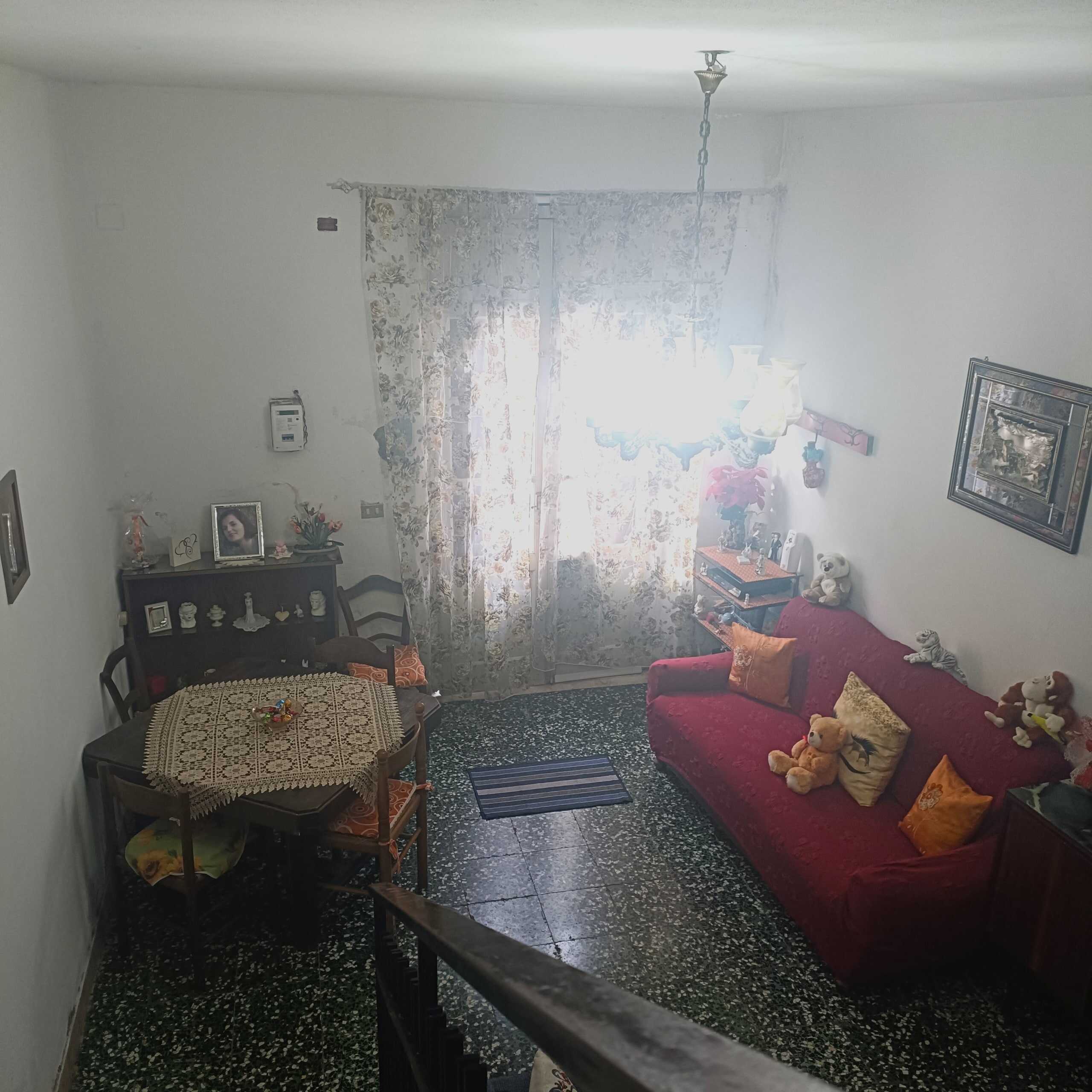 Divano rosso in soggiorno con decorazioni e giocattoli, lampadario antico, tende floreali, mobili in legno, dettagli casalinghi, casa NextCasa, immobili residenziali Italia, arredamento abitazioni, appartamento accogliente, vendita e affitto immobili.