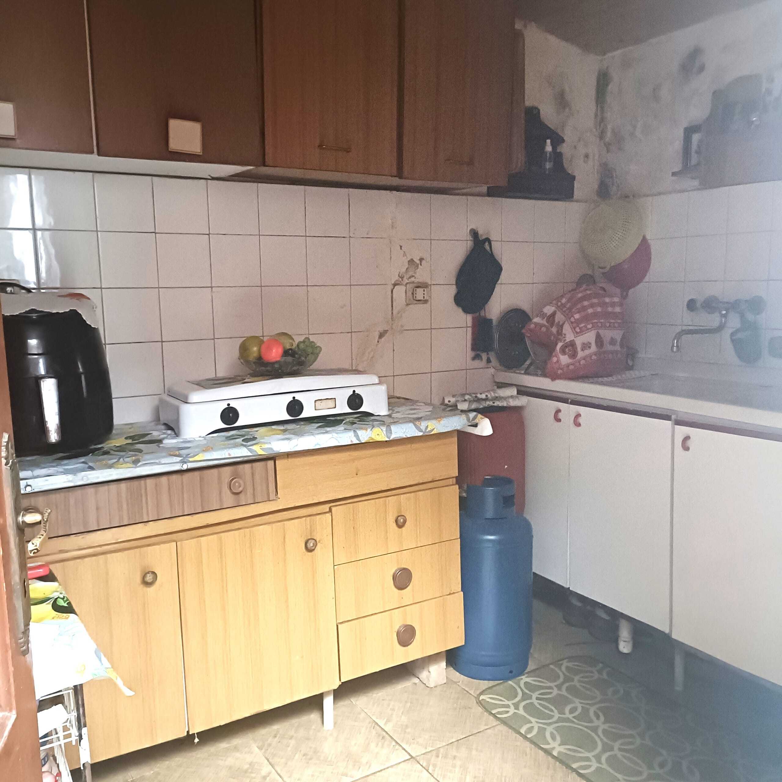 Vecchia cucina in stile rustico, mobili in legno e cucina a gas, piastrelle bianche e decorazioni casalinghe, ambiente semplice e funzionale, ideale per la vita quotidiana.