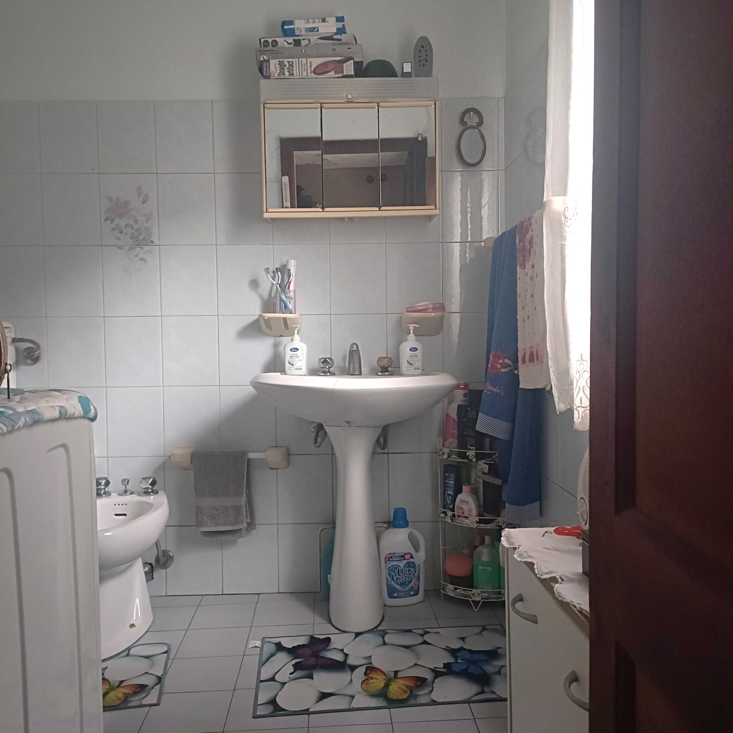 Lavabo e bidet in bagno con piastrelle bianche, accessori e prodotti per l'igiene personale.