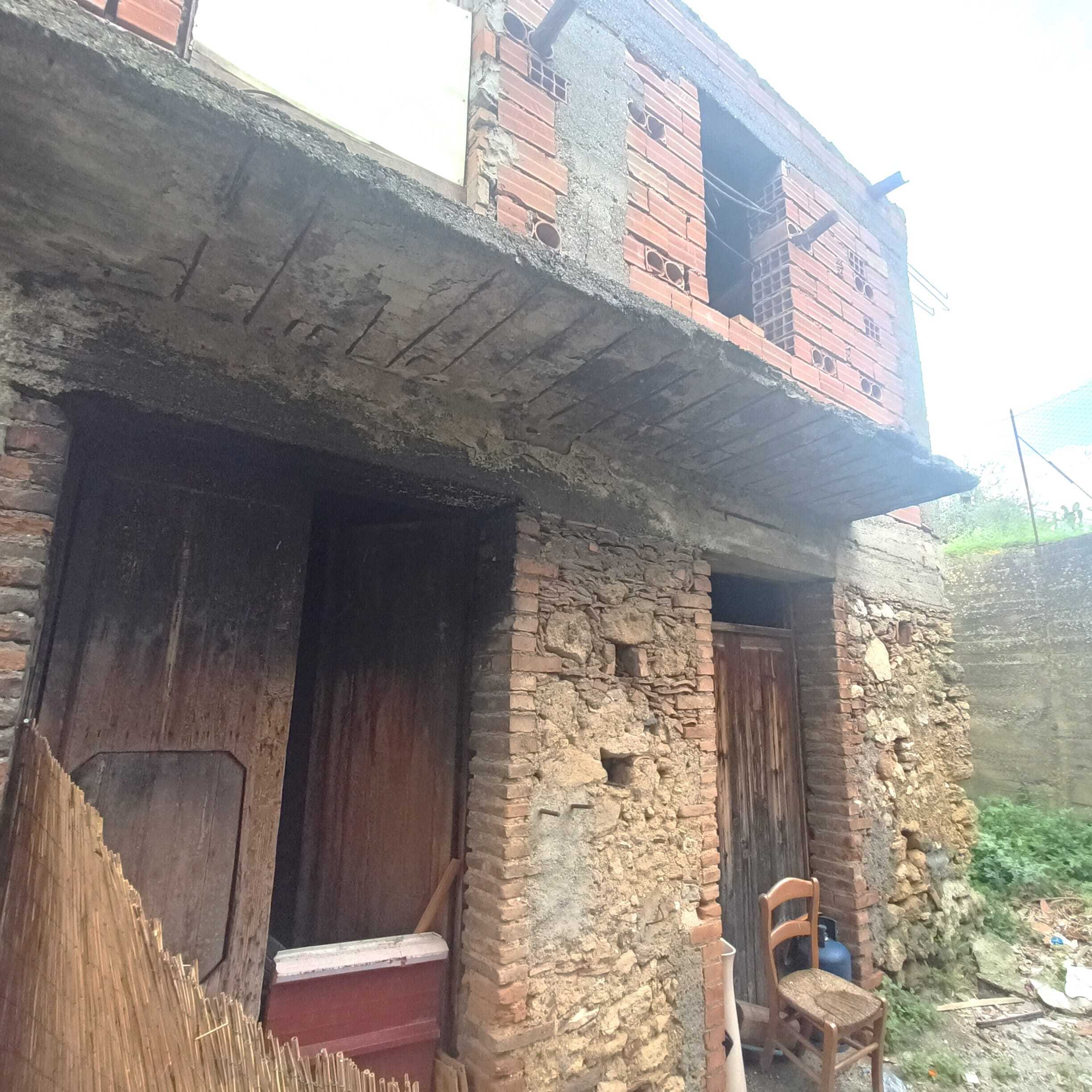Vecchia casa in costruzione con struttura in mattoni e cemento, pronto per ristrutturare, con ingressi e balcone in legno, scenario di edilizia tradizionale e ristrutturabile, ideale per intervento immobiliare.